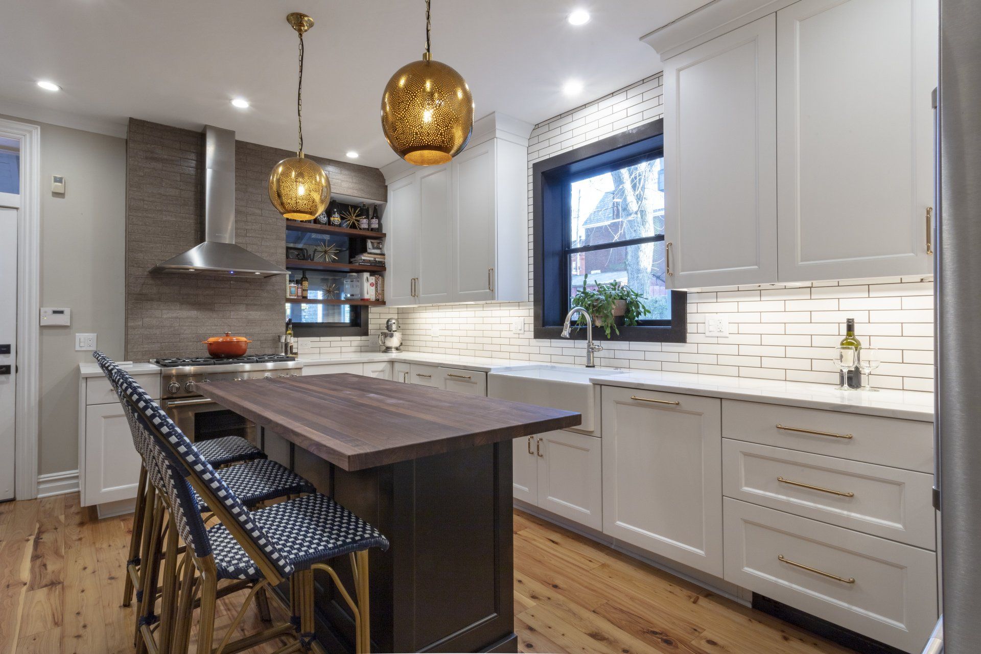 Modern white kitchen with dark island, pendant lights, bar stools, and hardwood floors
