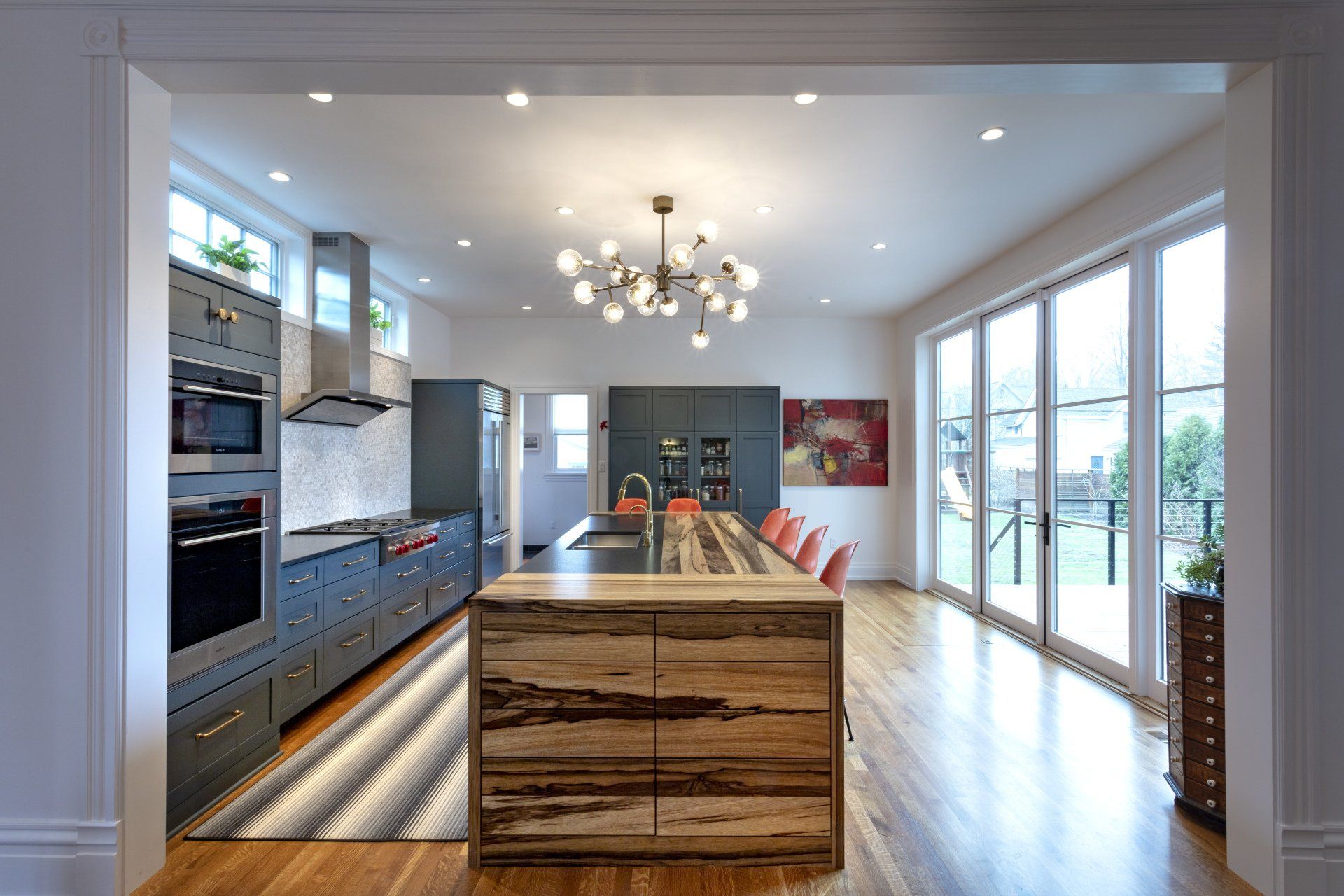 Modern kitchen with island, blue cabinetry, hardwood floors, and large windows overlooking a patio