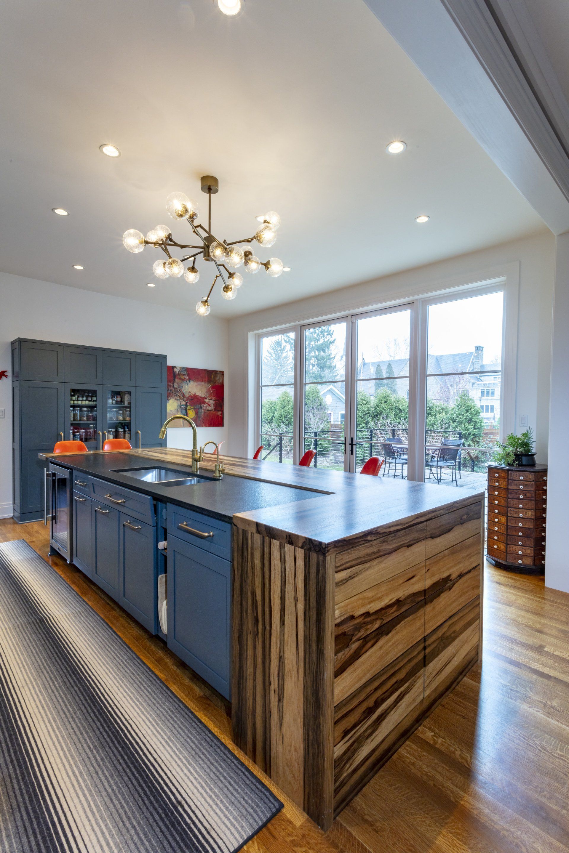 Modern kitchen with dark island, chandelier, and large windows overlooking a patio