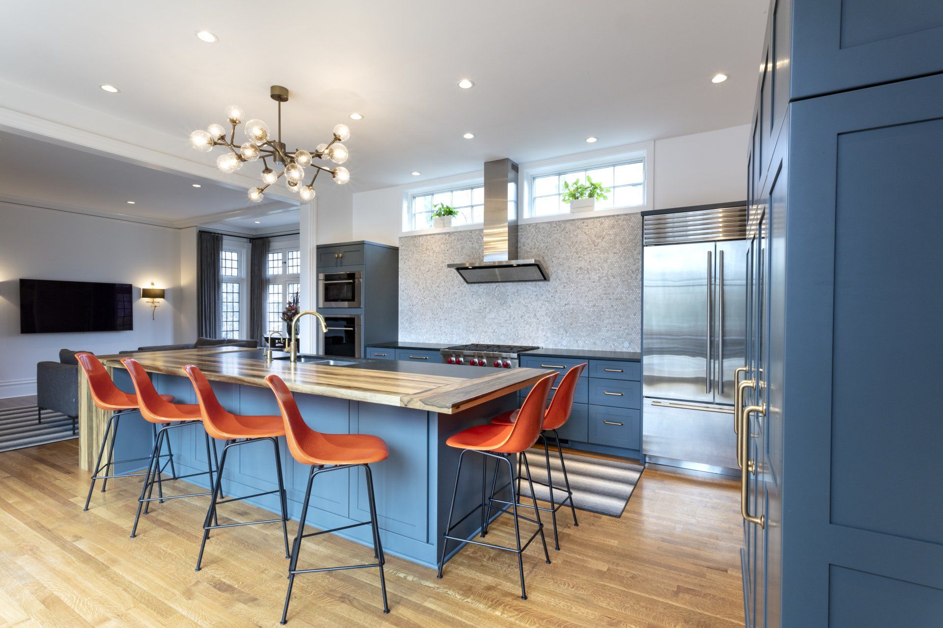 Modern kitchen with blue island, orange bar stools, stainless appliances, and chandelier lights