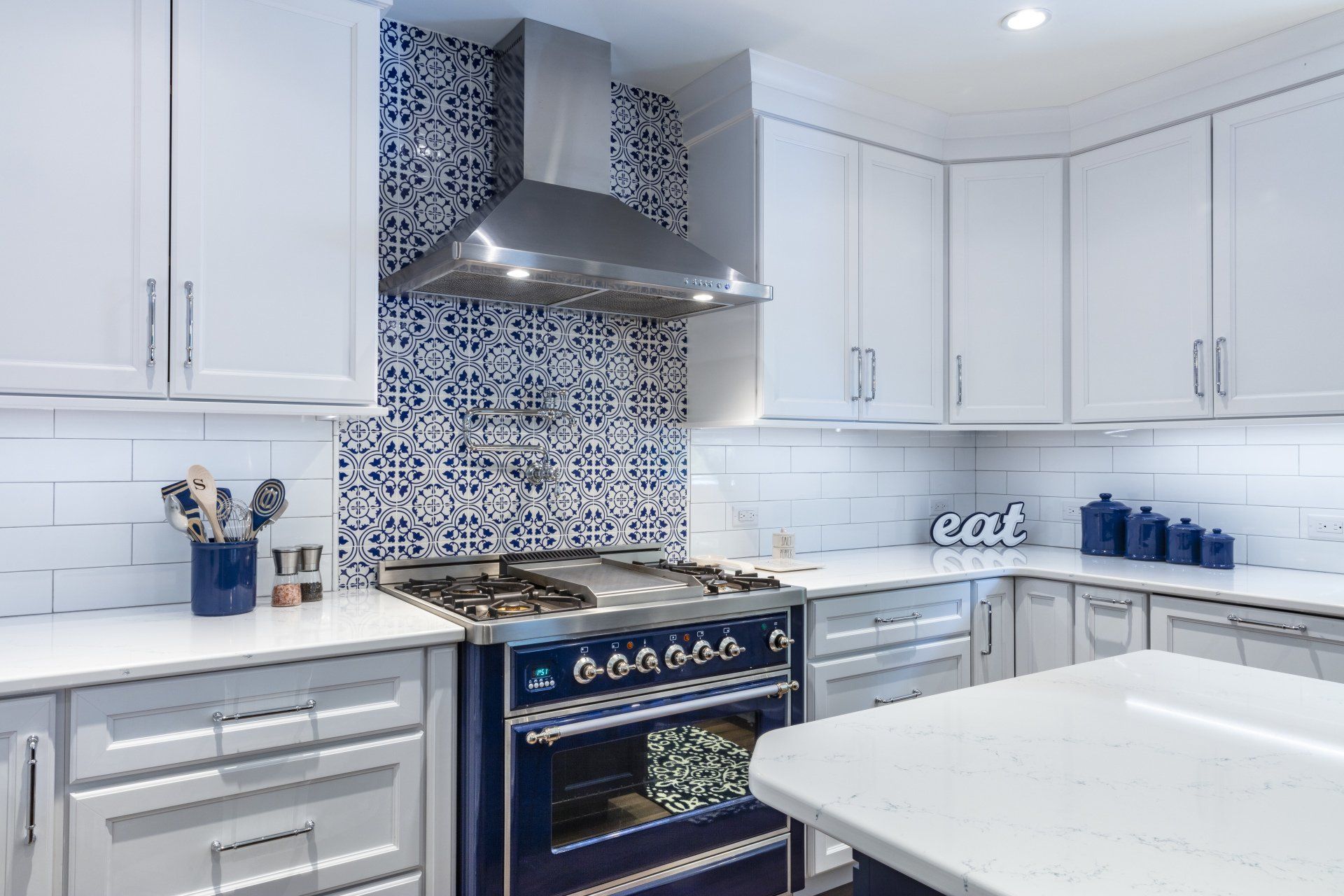 Bright white kitchen with blue patterned backsplash, navy stove, and white countertops