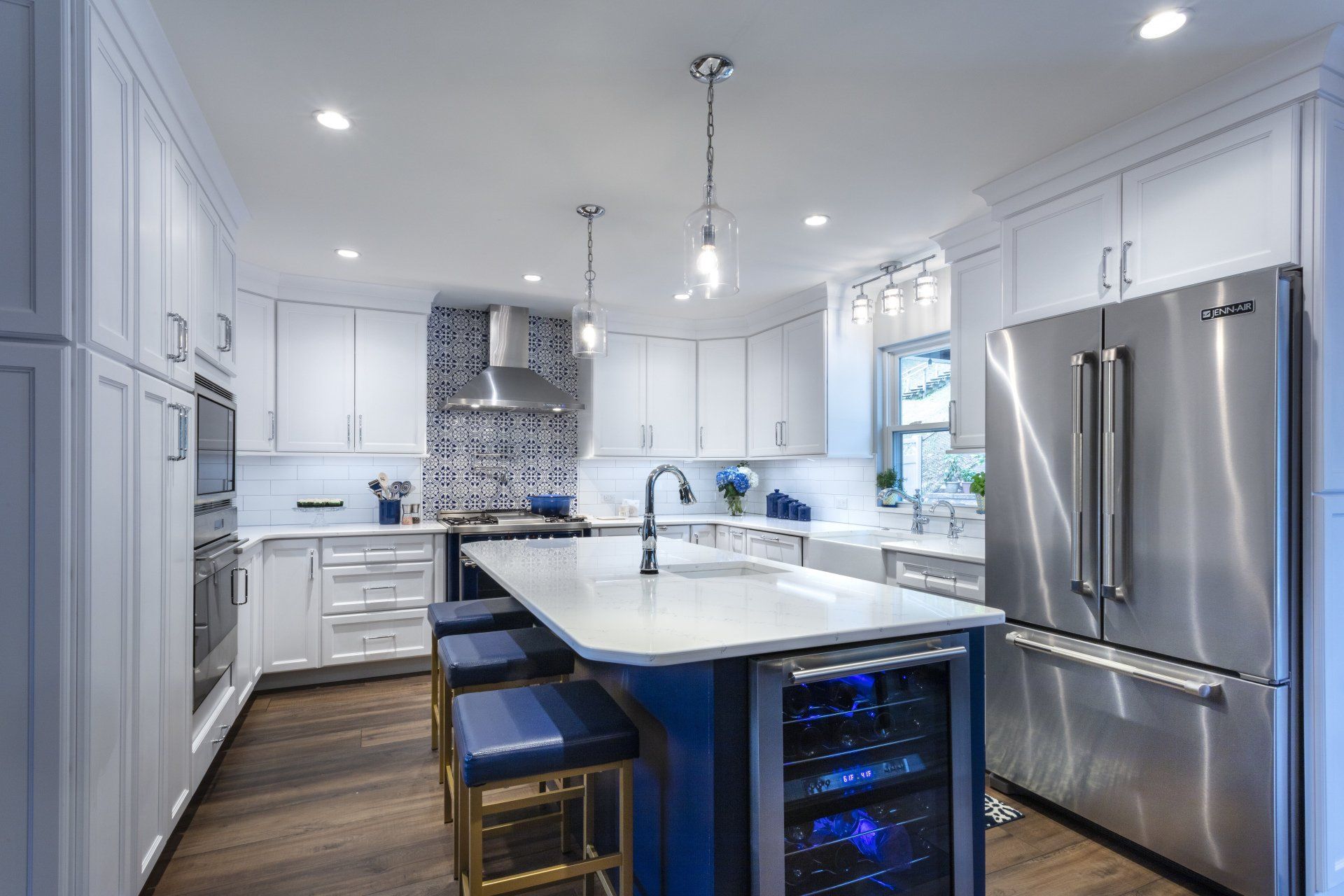 Modern white kitchen with island, stainless steel appliances, blue stools, and glass-front wine cooler