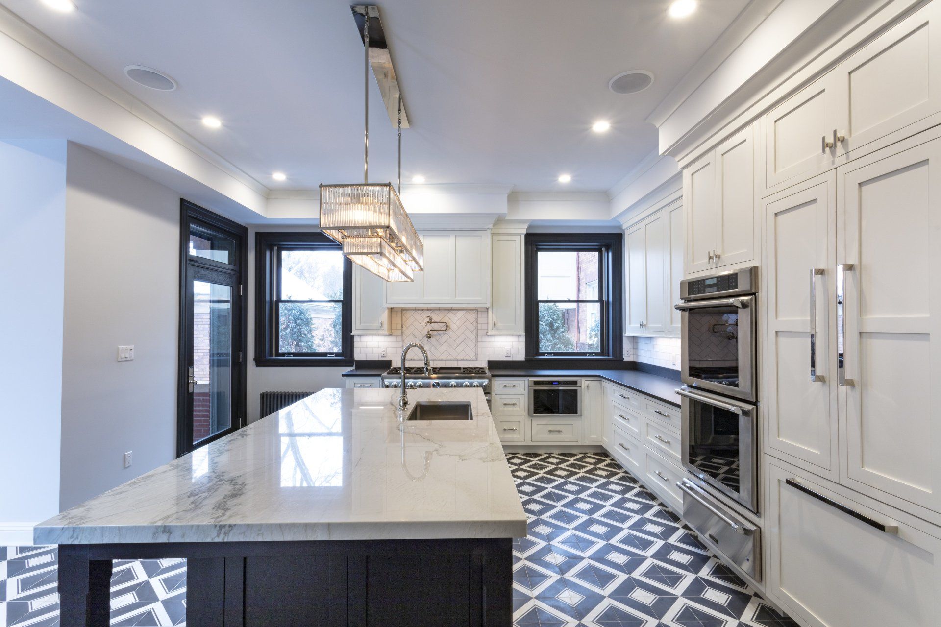 Modern white kitchen with marble island, pendant light, black-framed windows, and patterned tile floor
