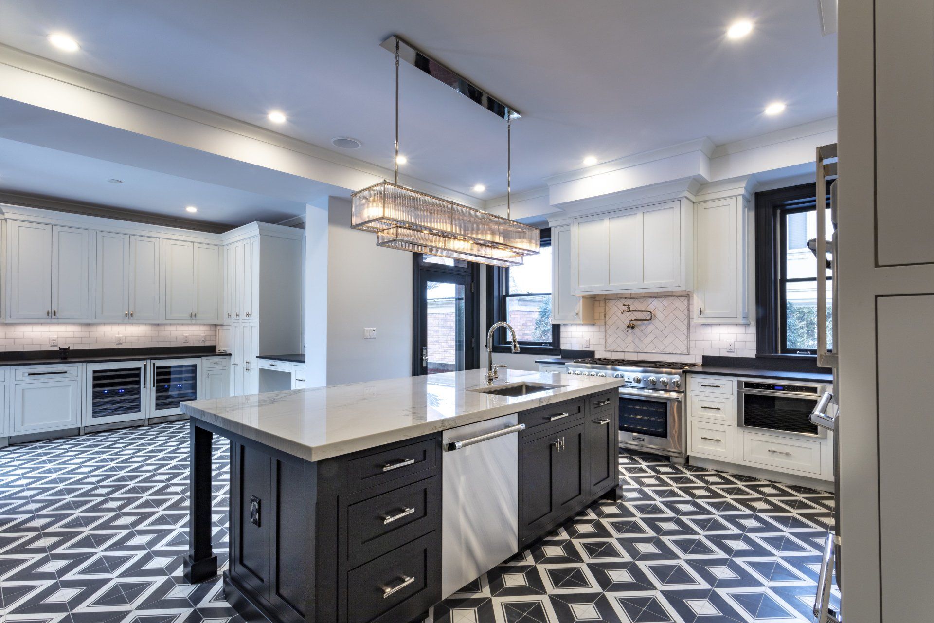 Bright modern kitchen with white cabinets, black island, geometric floor, and stainless appliances.
