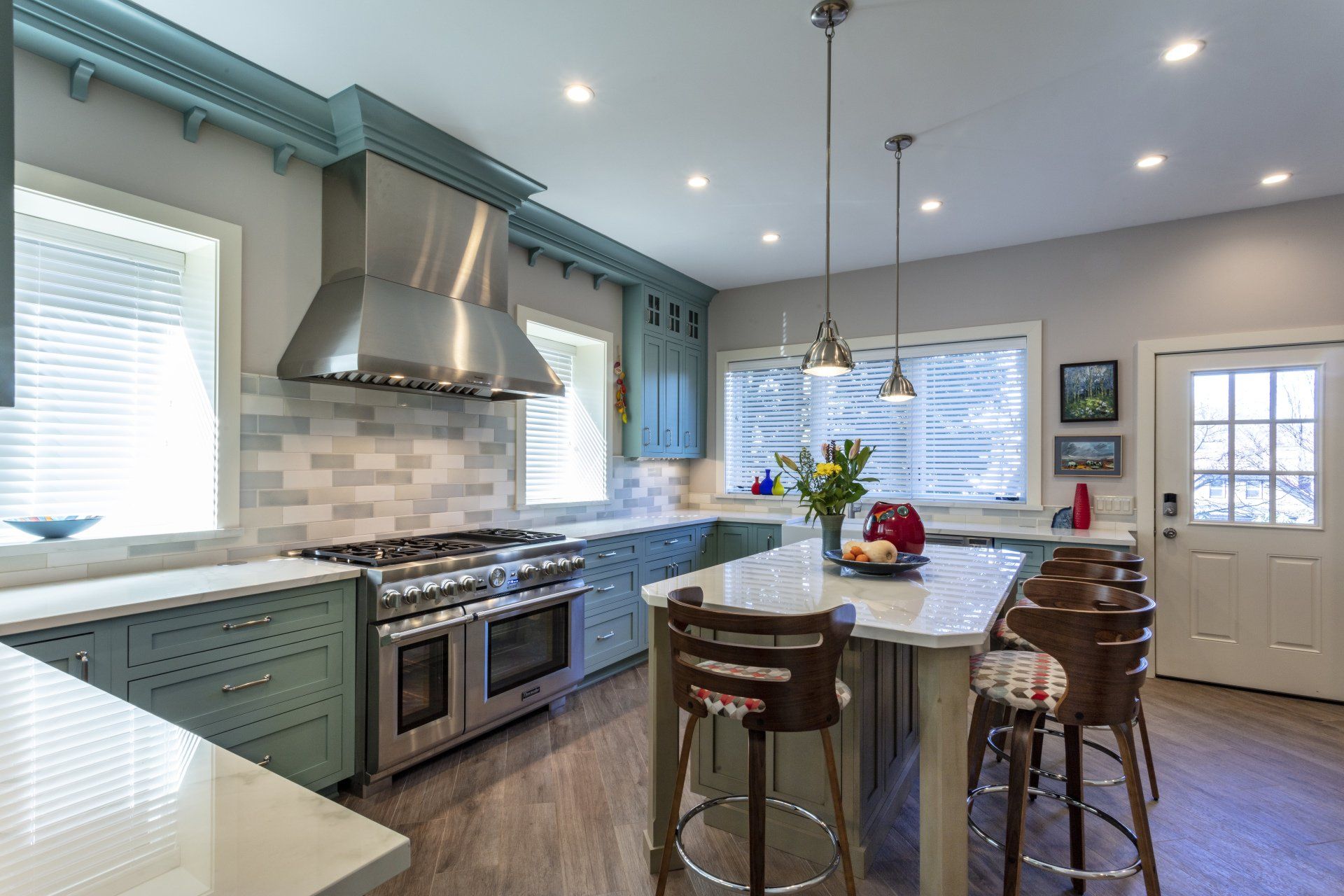 Bright, modern kitchen with stainless stove, island seating, teal cabinets, and white tile backsplash