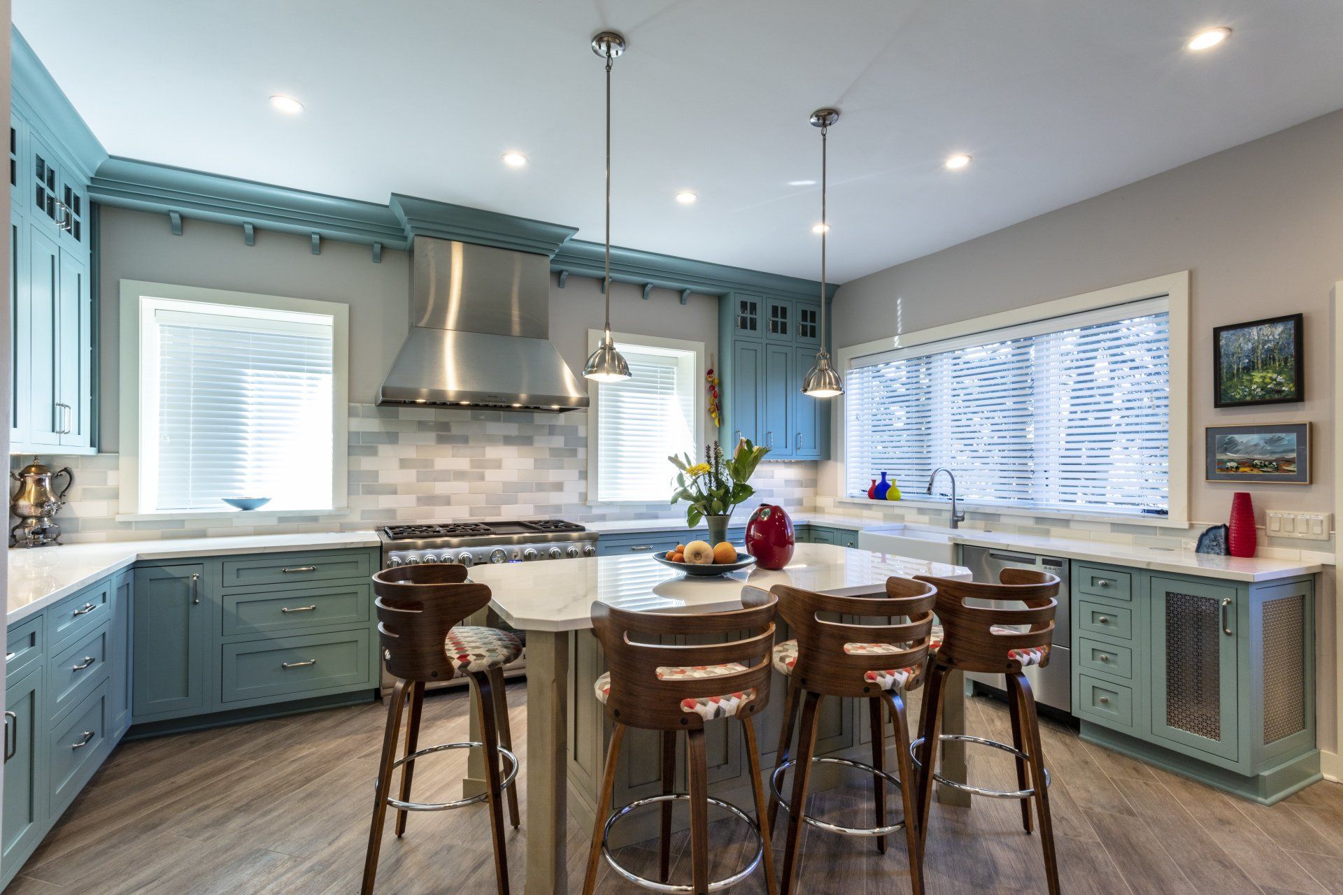 Bright kitchen with teal cabinets, island seating, stainless range hood, and large windows