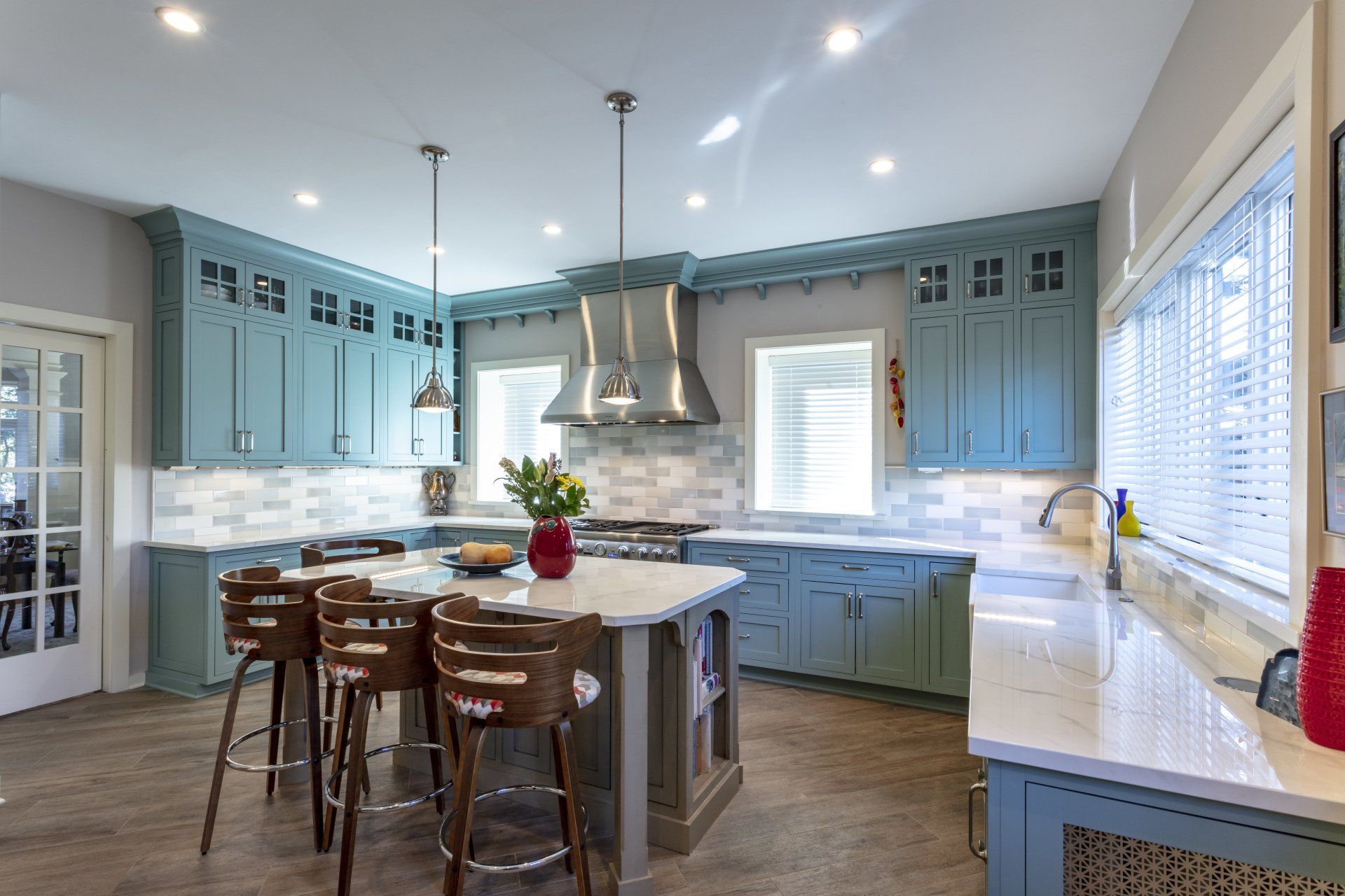 Bright blue kitchen with island, bar stools, white countertops, and stainless-steel range hood