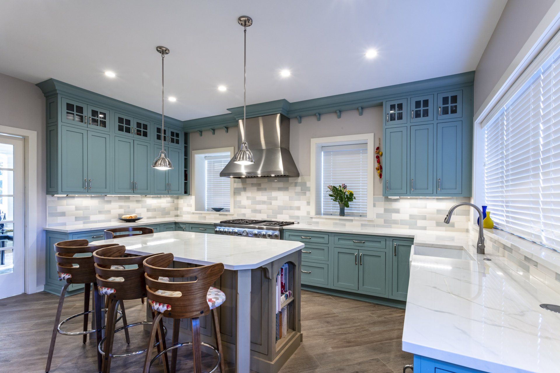 Bright kitchen with teal cabinets, white marble counters, large island, and bar stools under pendant lights