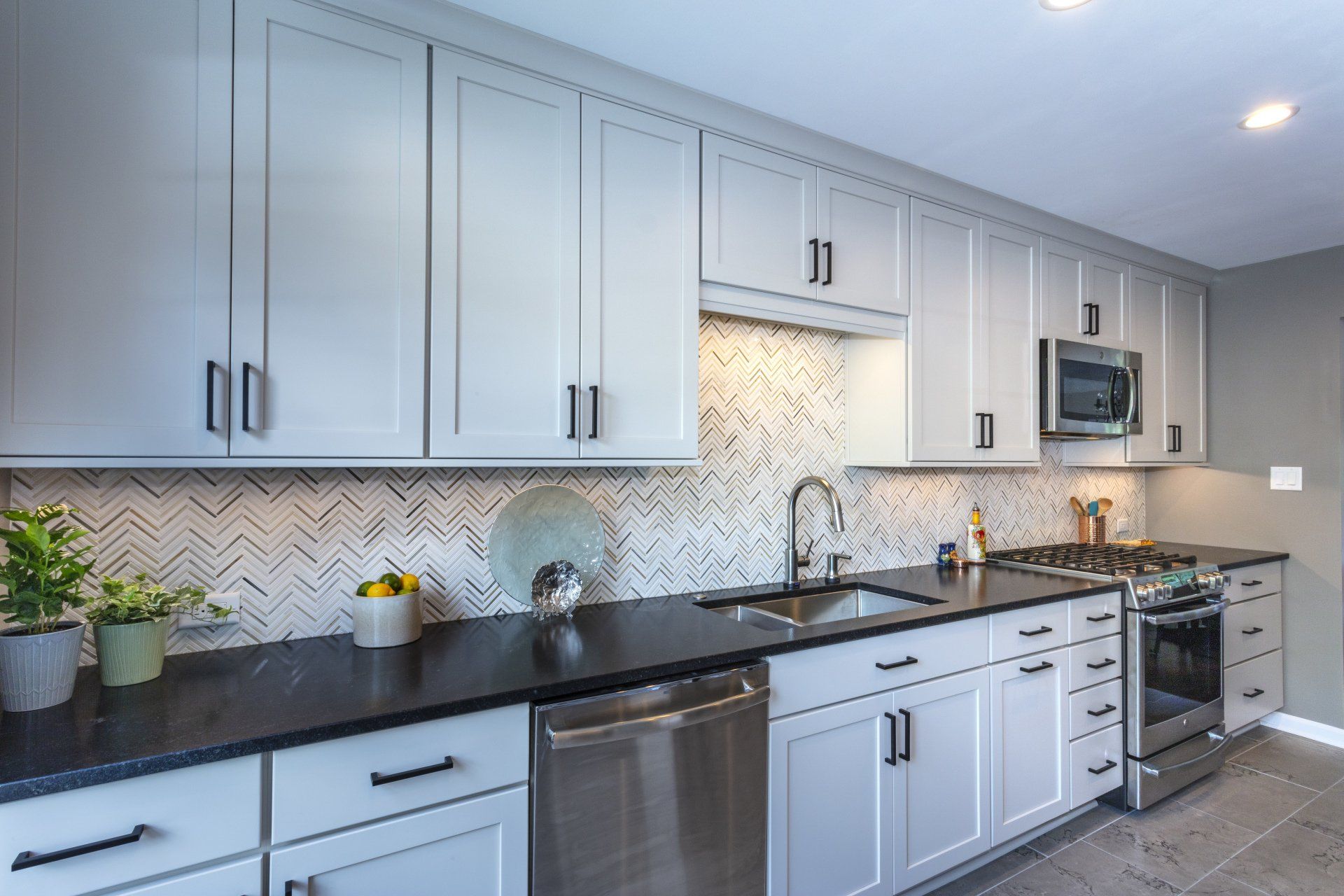 Modern kitchen with light gray cabinets, dark countertops, stainless appliances, and a tiled backsplash.