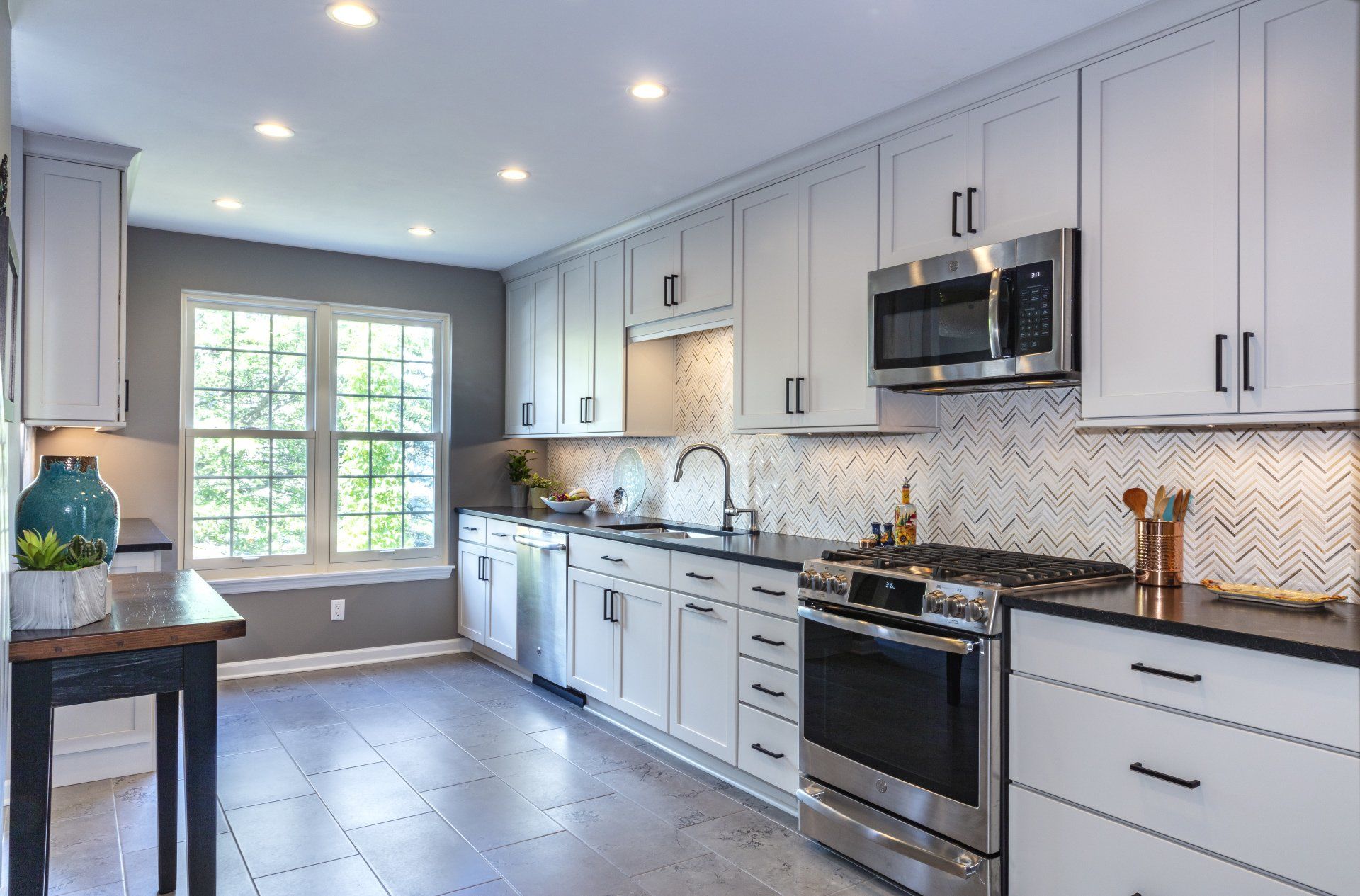 Modern white kitchen with black appliances, marble counters, and a bright window nook