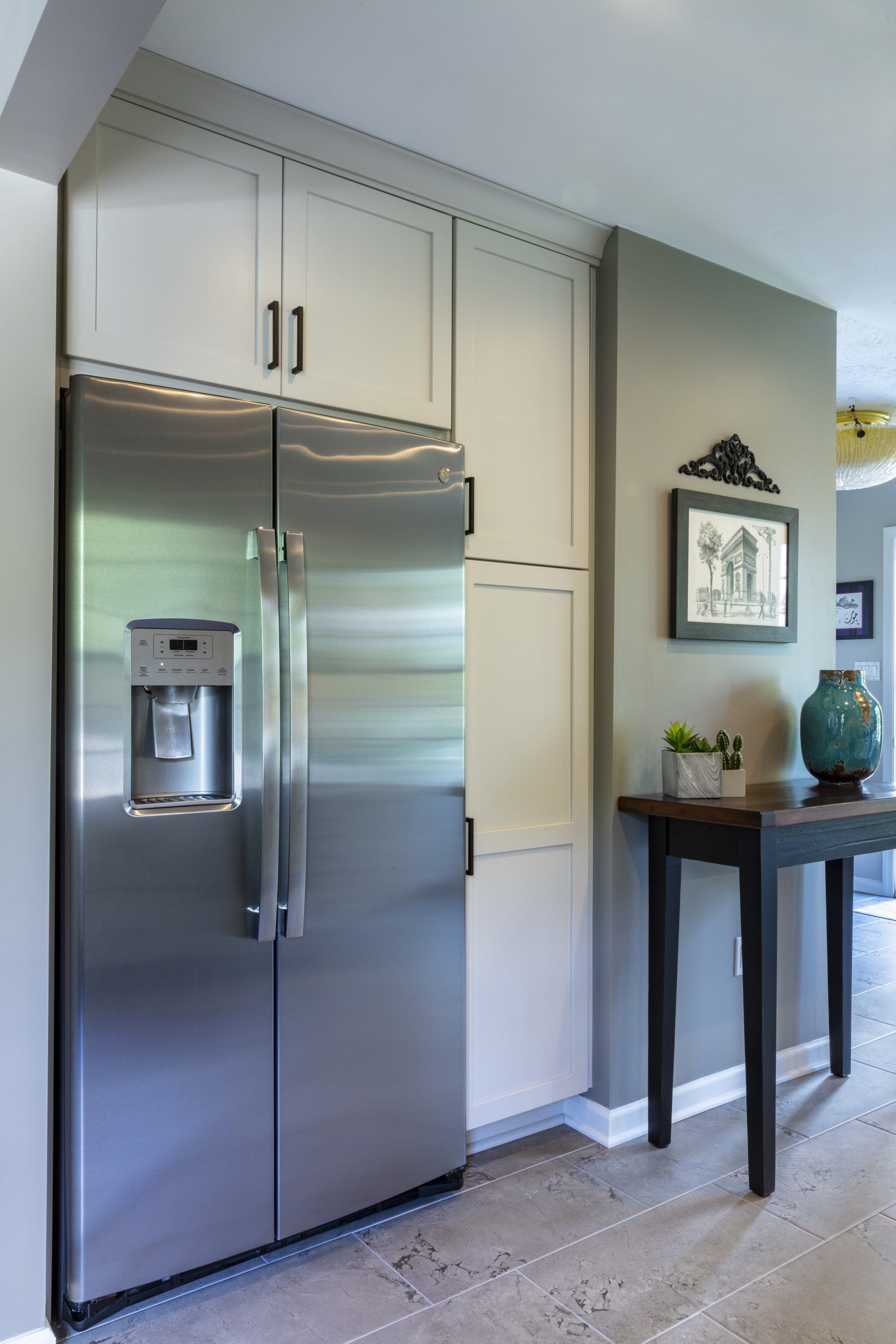 Stainless steel refrigerator beside white cabinets in a bright kitchen hallway