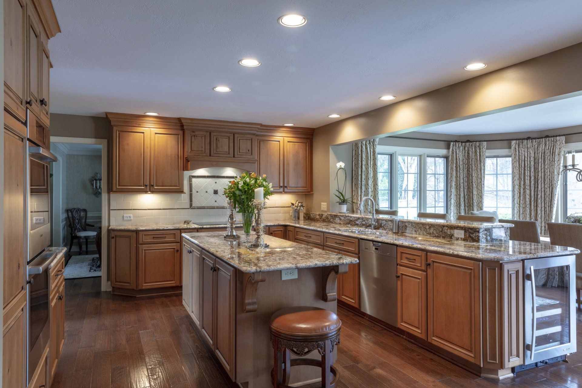Spacious kitchen with wood cabinets, granite island, and large windows overlooking a wooded view