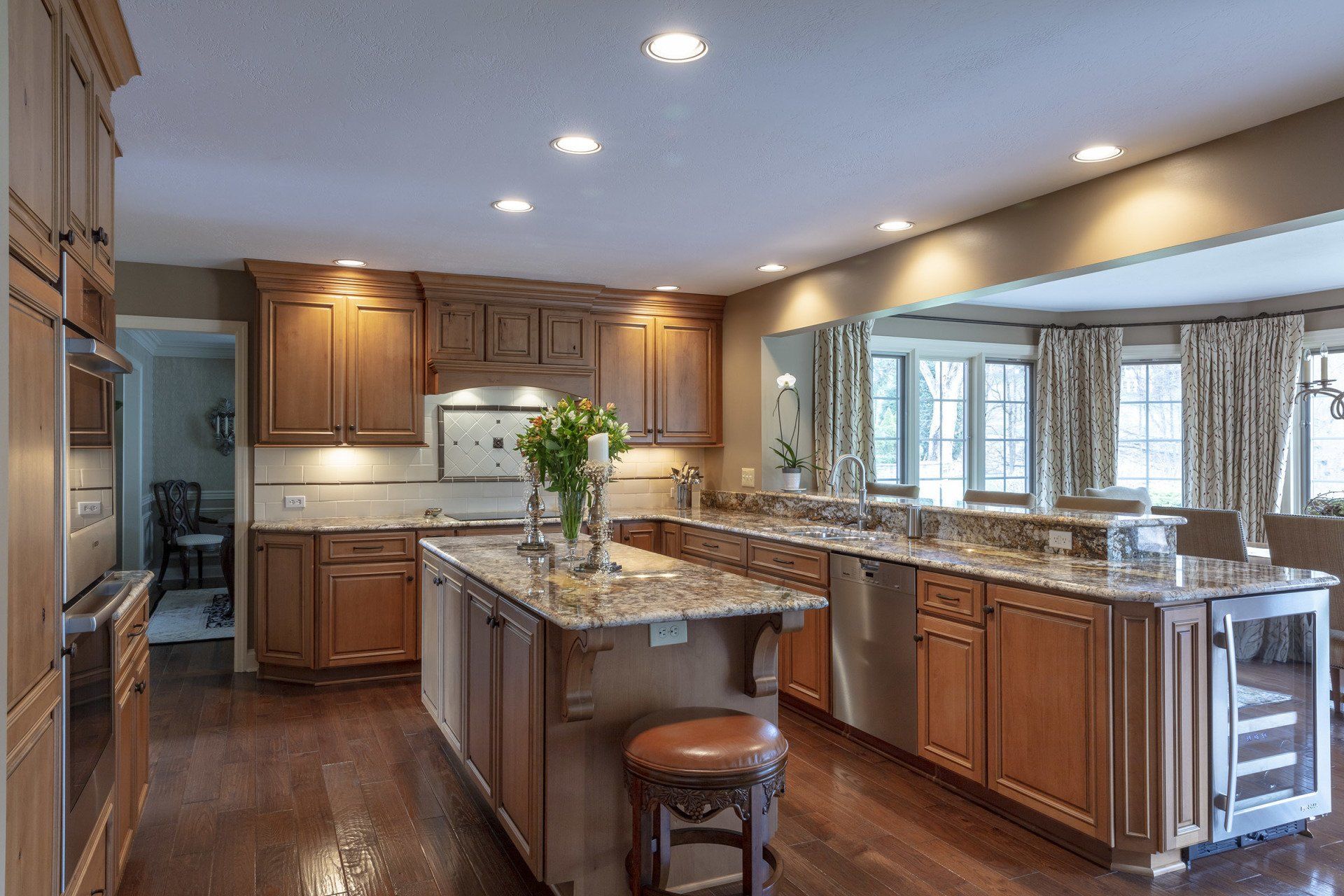 Modern kitchen with wood cabinets, granite island, stainless appliances, and large windows over a hardwood floor
