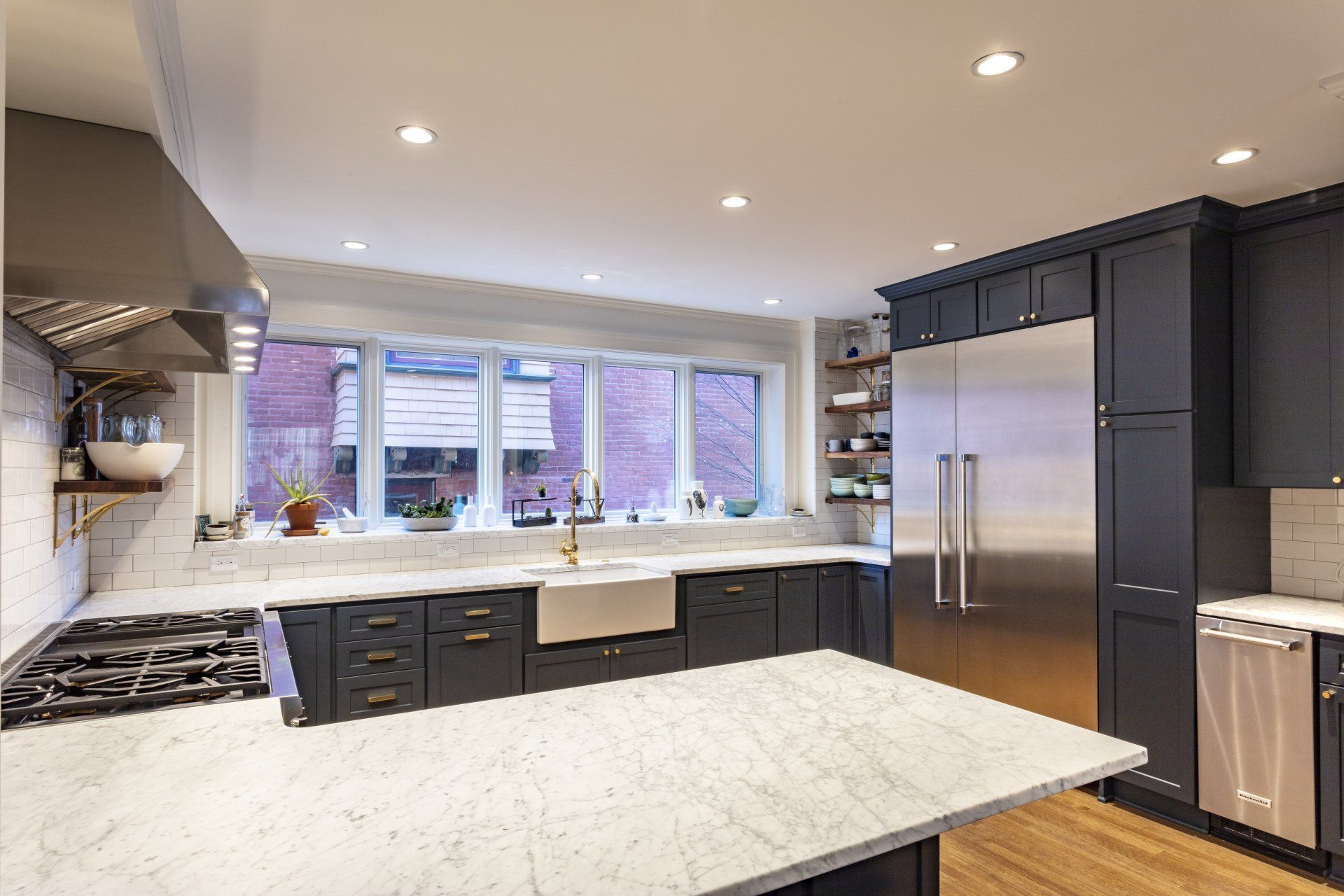Modern kitchen with white countertops, dark cabinets, stainless steel fridge, and a large window over the sink