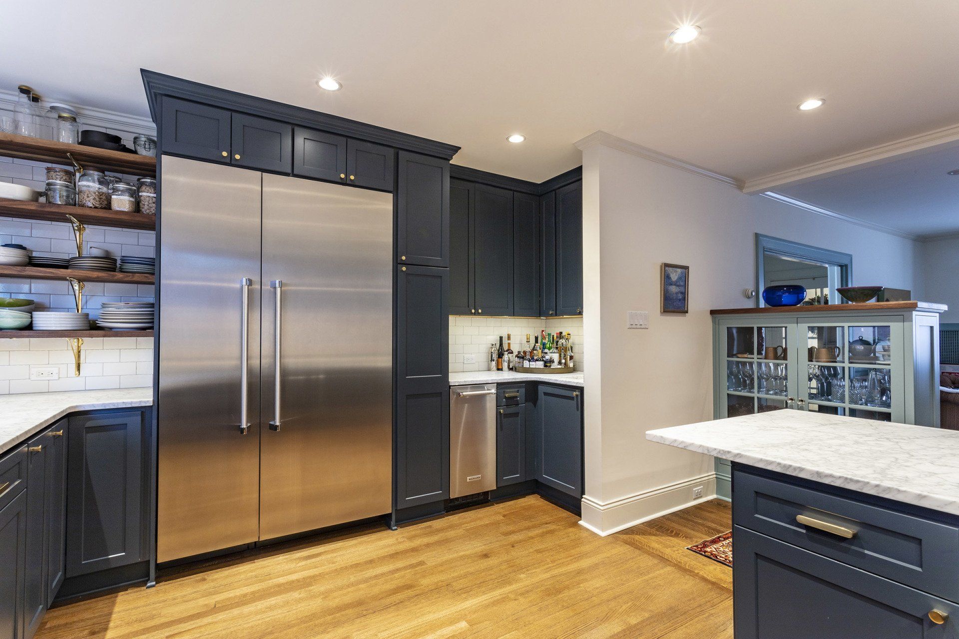 Modern kitchen with stainless steel refrigerator, navy cabinets, white island, and hardwood floors