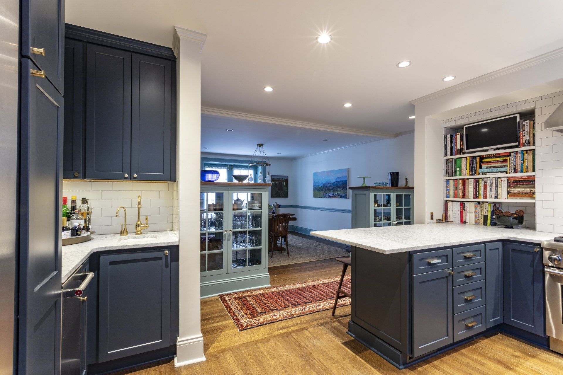 Modern navy-and-white kitchen with a large island, wood floors, and built-in shelving