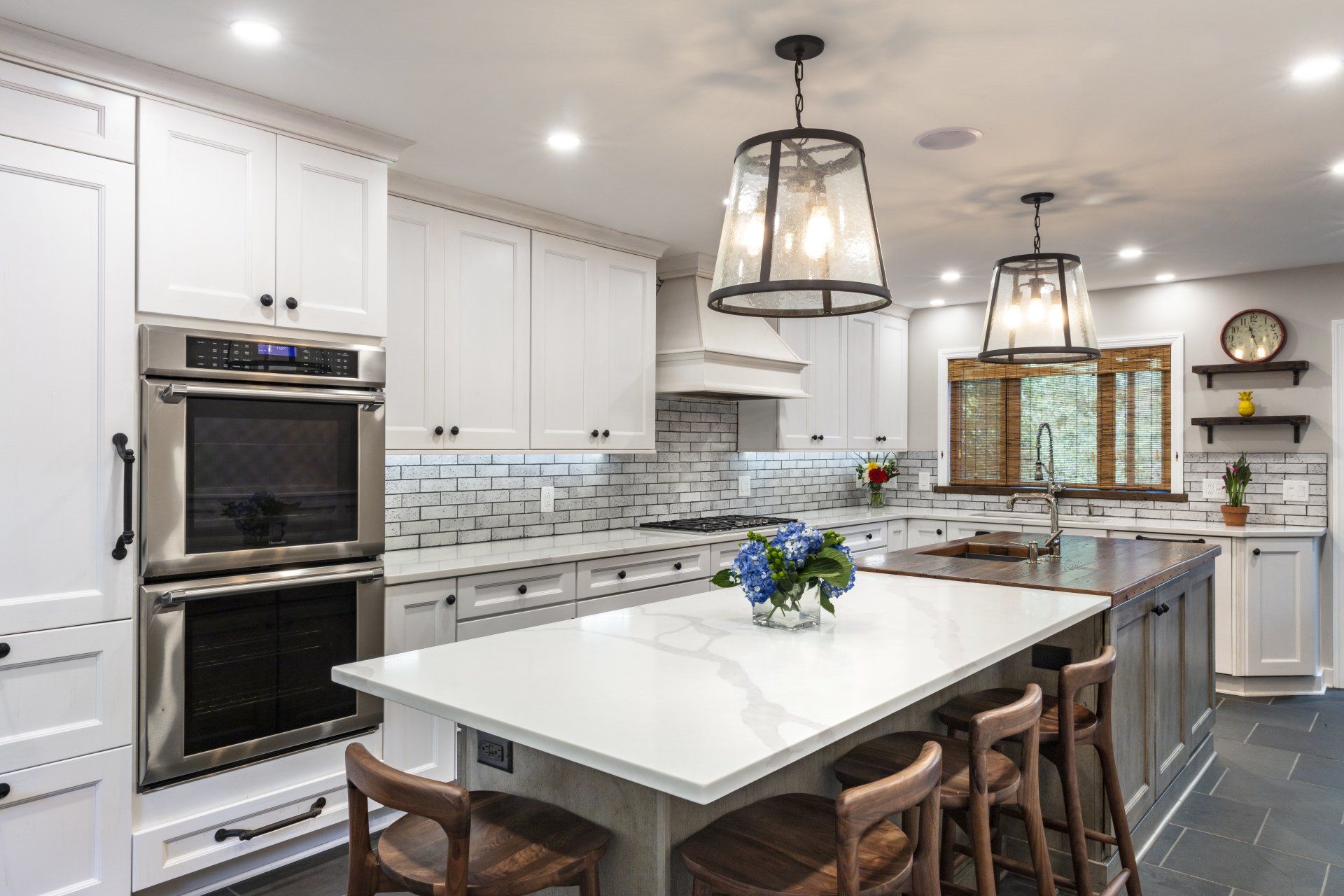 Bright modern white kitchen with large island, pendant lights, and gray tile floor.