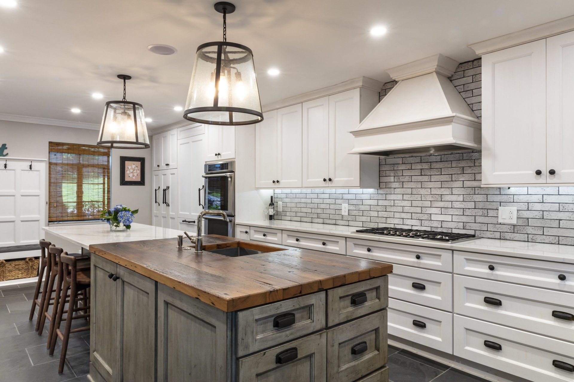 Bright white kitchen with a wooden island, pendant lights, and a gray tiled backsplash