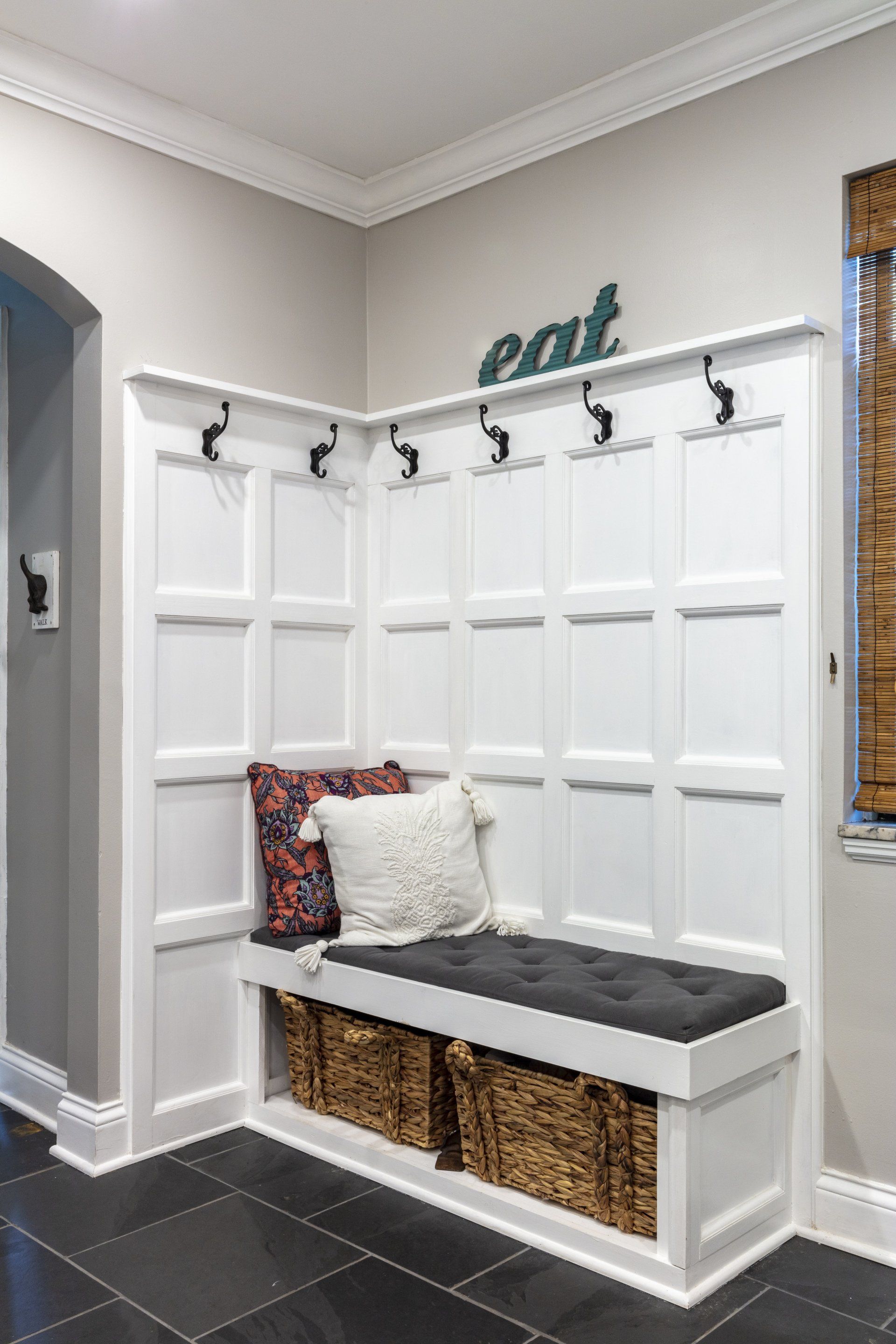 White entryway bench with coat hooks, cubbies, and patterned pillows against a gray wall