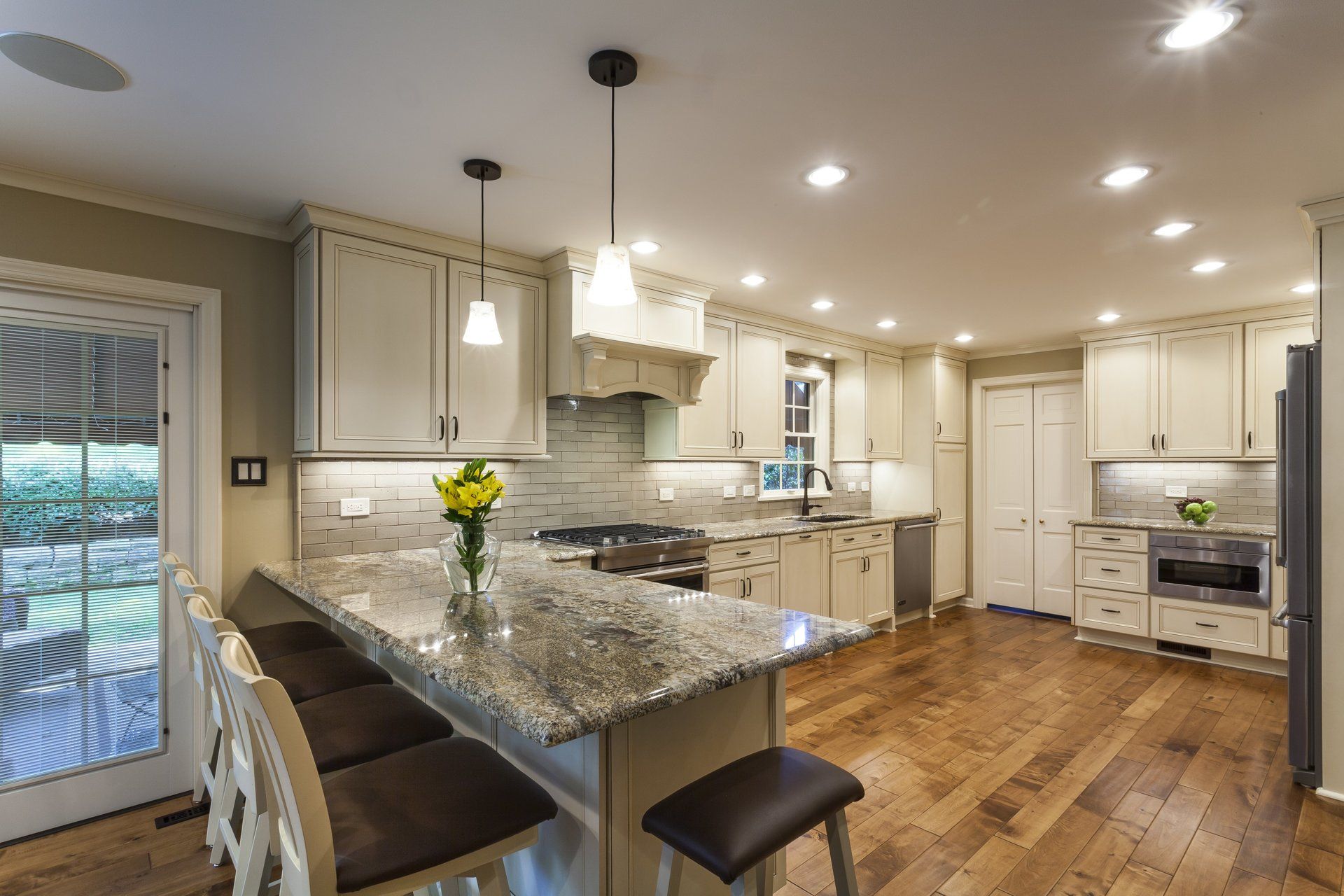 Bright modern kitchen with white cabinets, granite island, bar stools, and hardwood floors