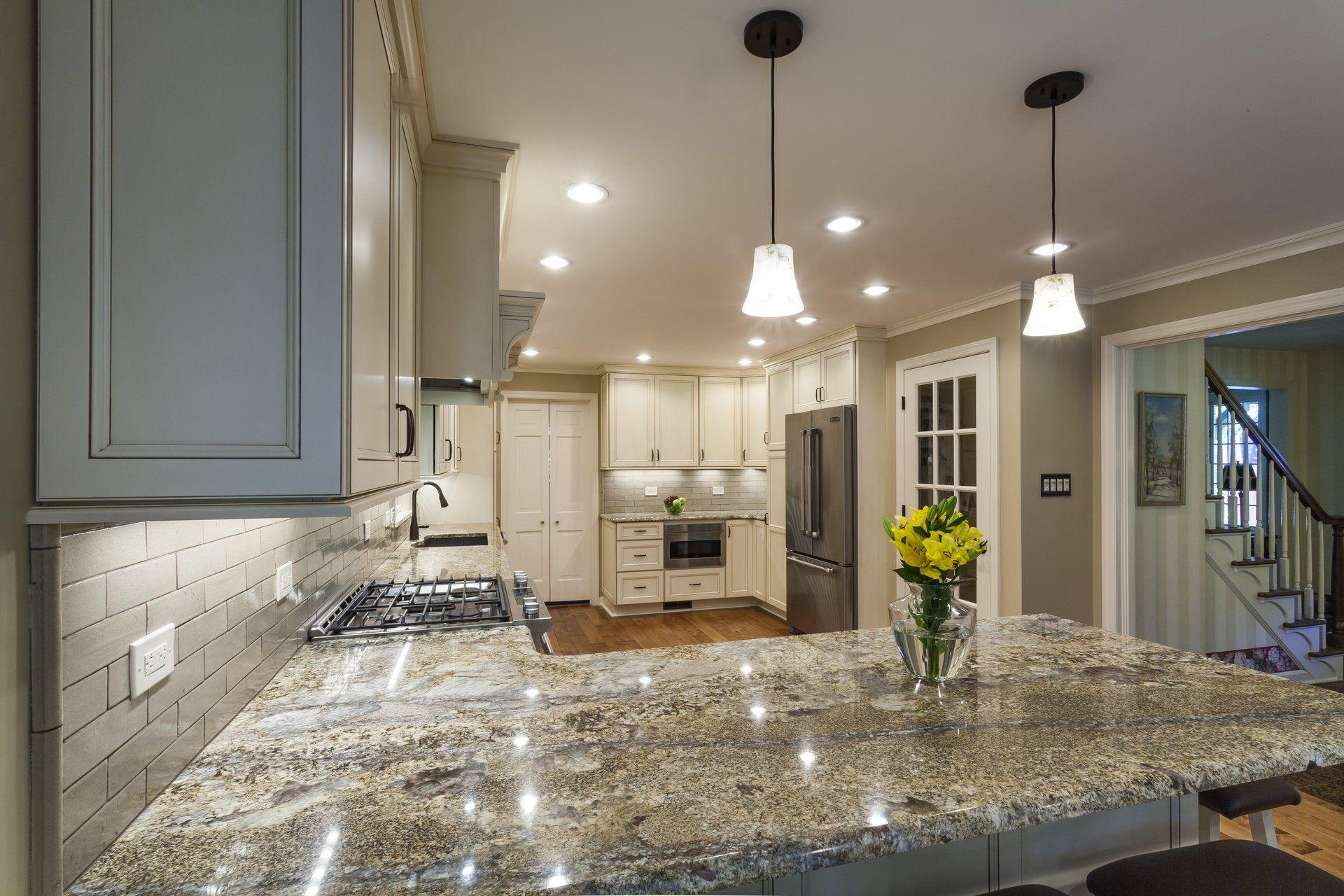 Bright kitchen with granite island, white cabinets, pendant lights, and a vase of yellow flowers.