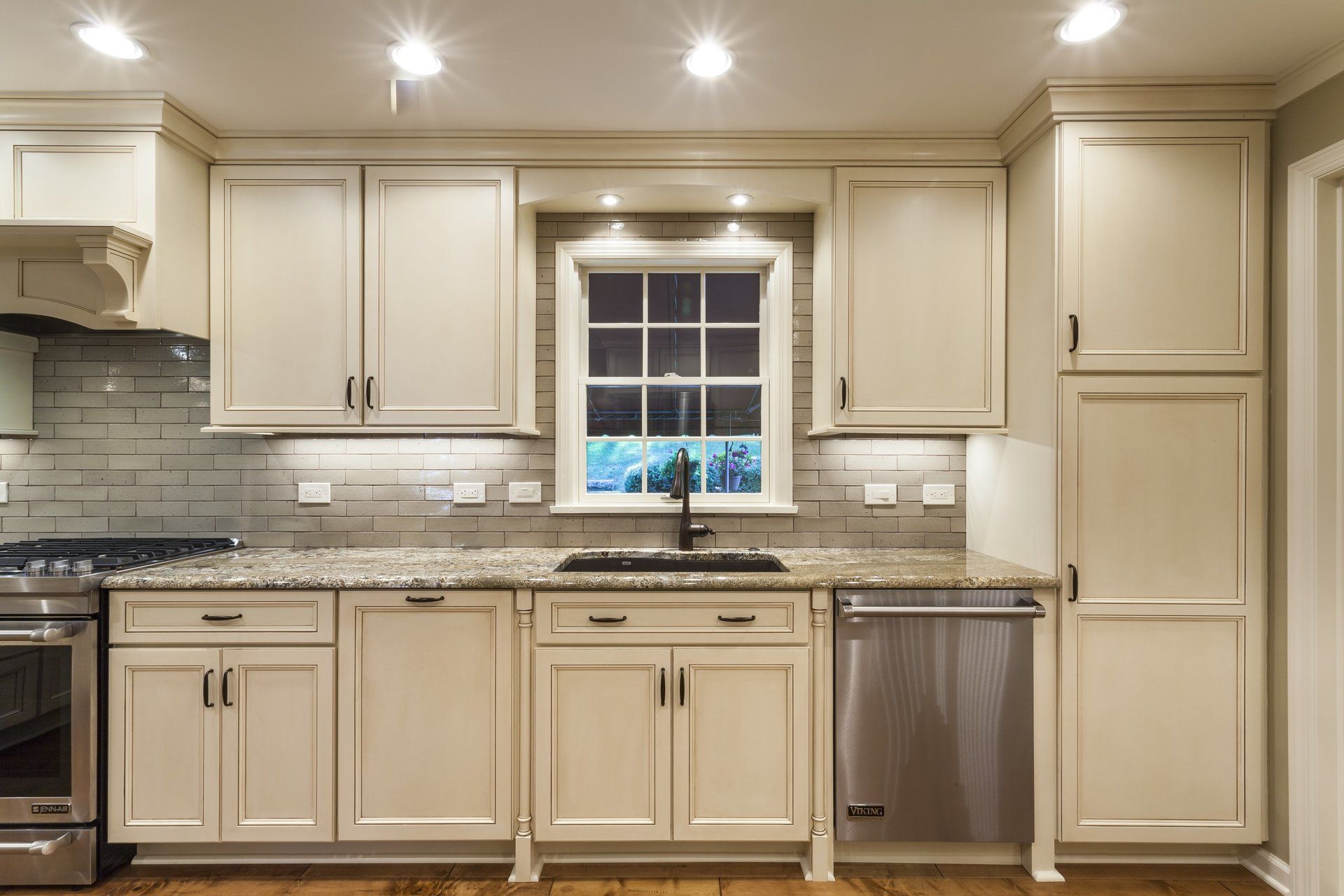 Bright cream kitchen with granite countertops, stainless dishwasher, and window above the sink