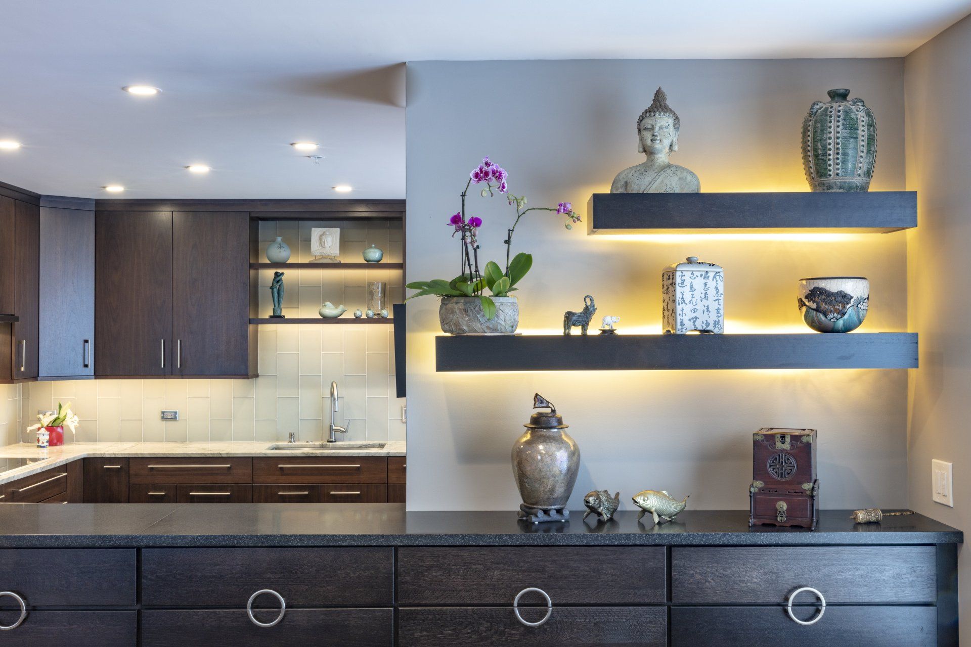 Modern living room with dark cabinets, lit shelves, Buddha statues, and orchids under warm lighting