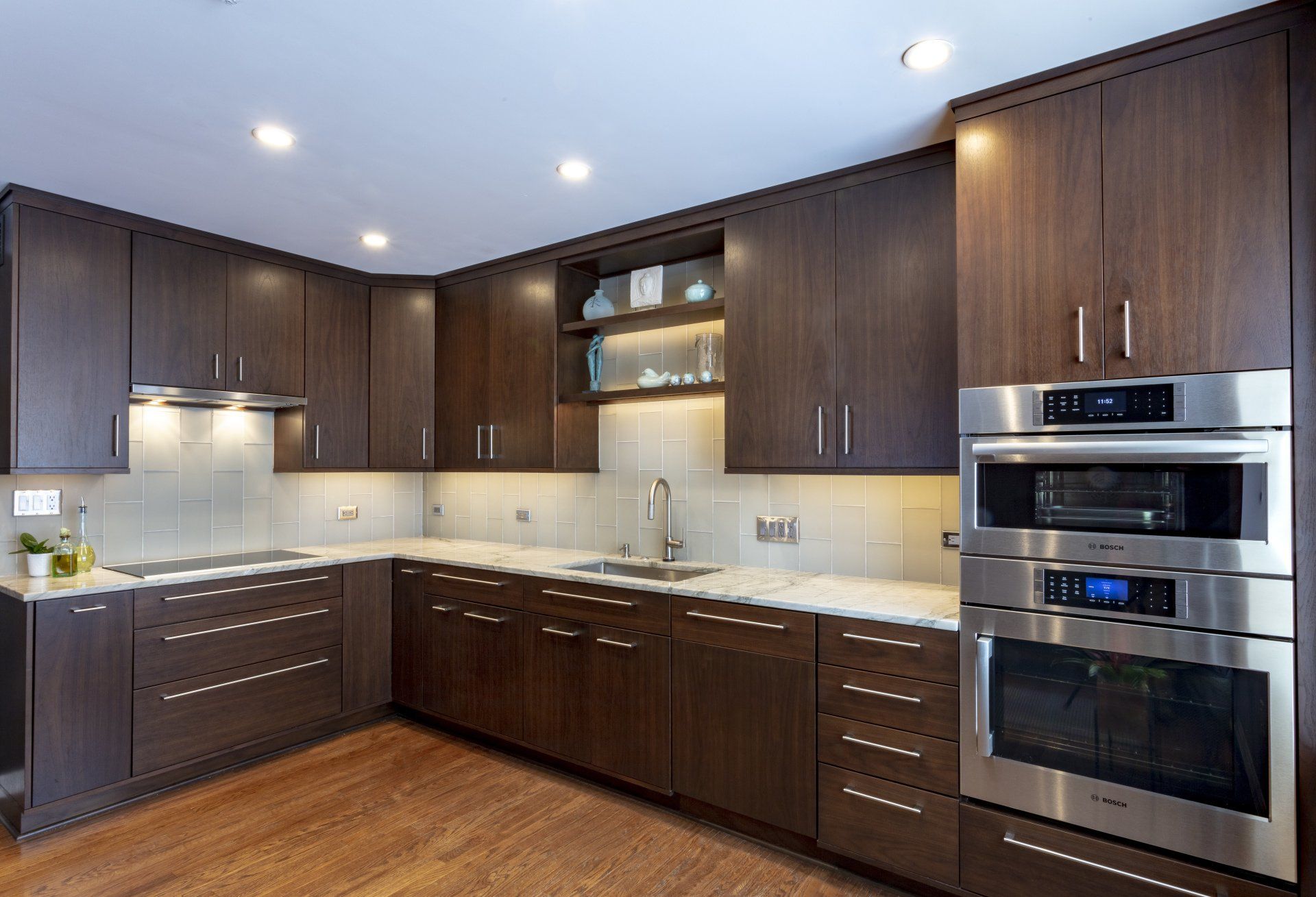Modern kitchen with dark wood cabinets, stainless steel appliances, white countertops, and wood floors.
