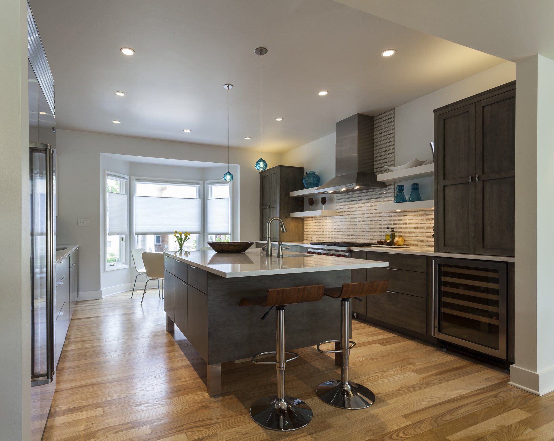 Modern kitchen with dark cabinets, large island, wood floors, and bright recessed lighting.