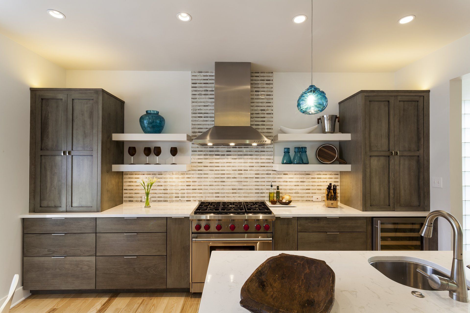 Modern kitchen with dark wood cabinets, stainless steel range hood, white tile backsplash, and blue pendant lights