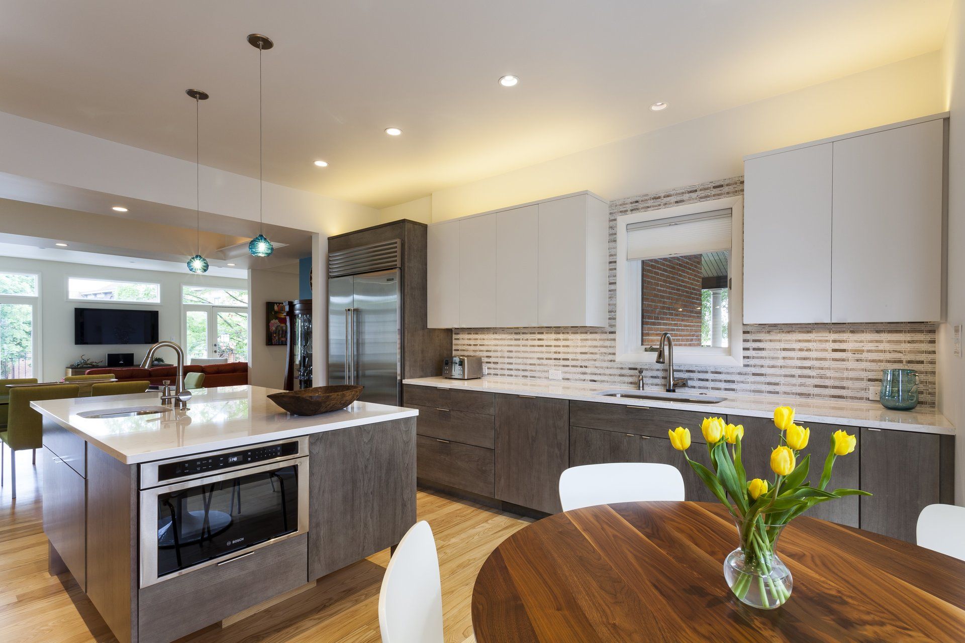 Modern kitchen with island, gray cabinets, stainless fridge, and dining table with yellow flowers
