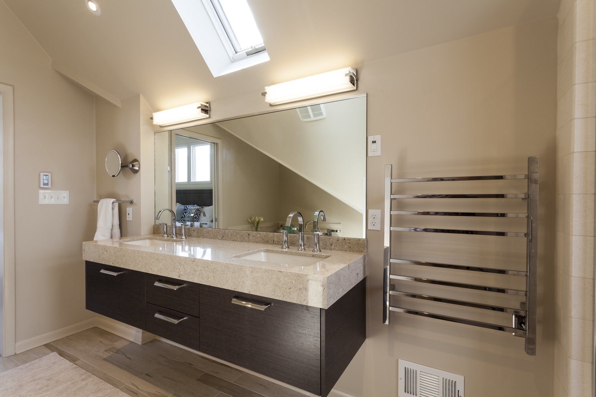 Modern beige bathroom with double vanity, large mirror, and chrome towel warmer.