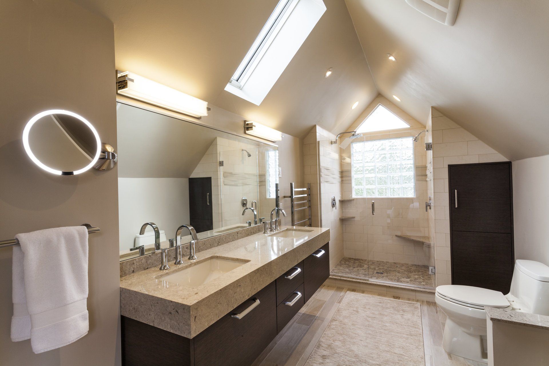 Modern bathroom with double vanity, large mirror, skylights, and a walk-in shower.
