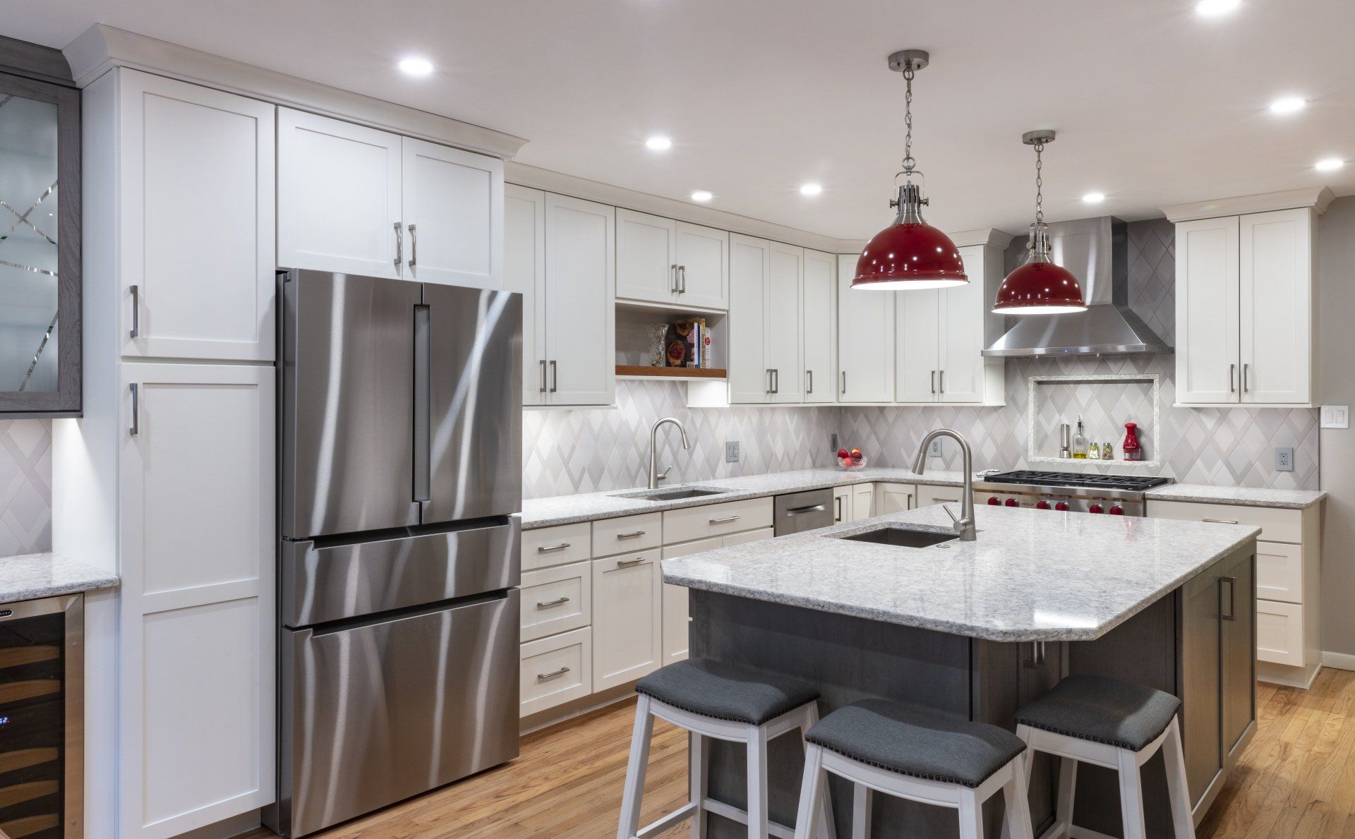 Modern kitchen with white cabinets, stainless fridge, marble island, and red pendant lights