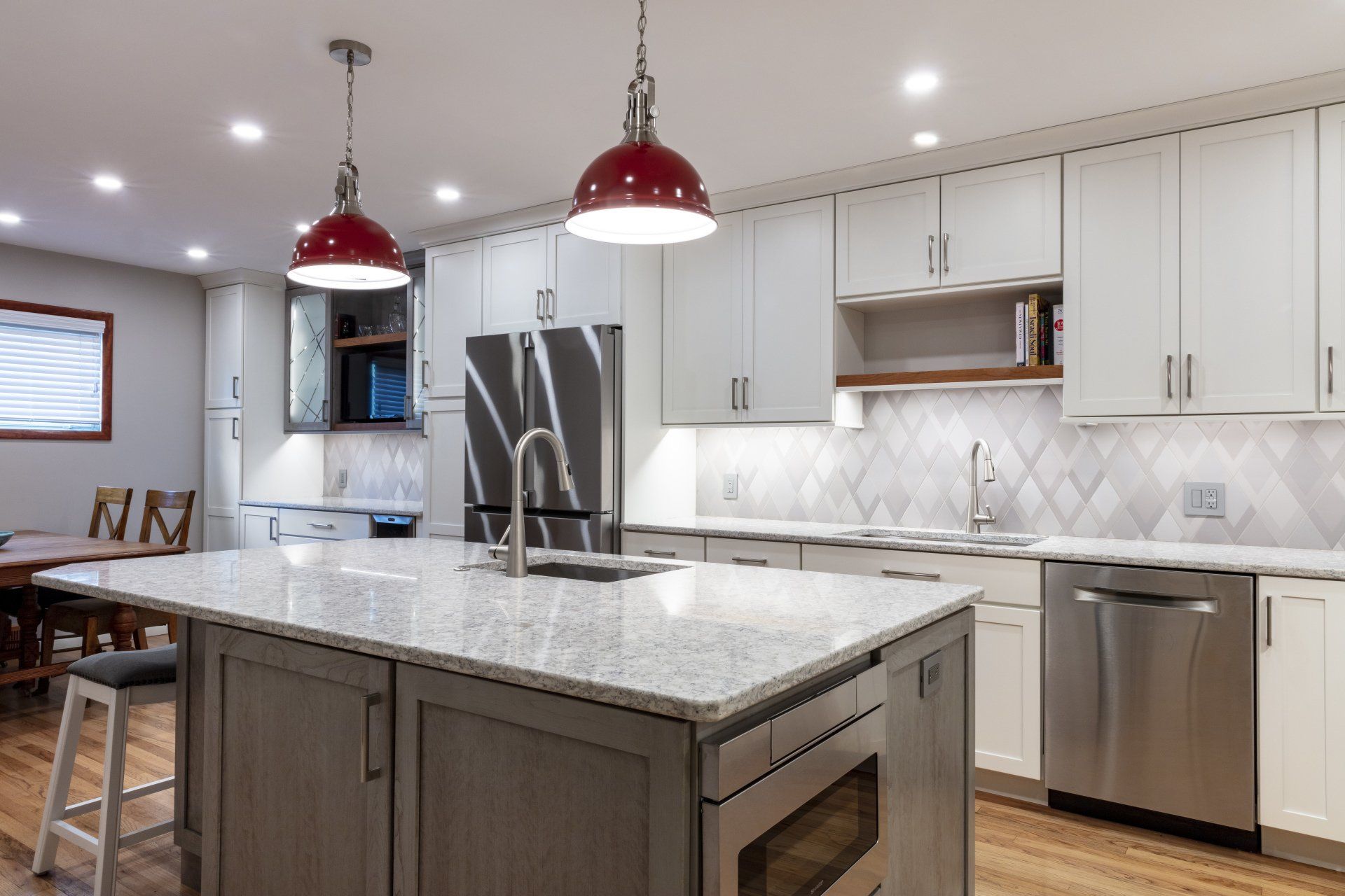 Modern kitchen with white cabinets, gray island, stainless appliances, and red pendant lights