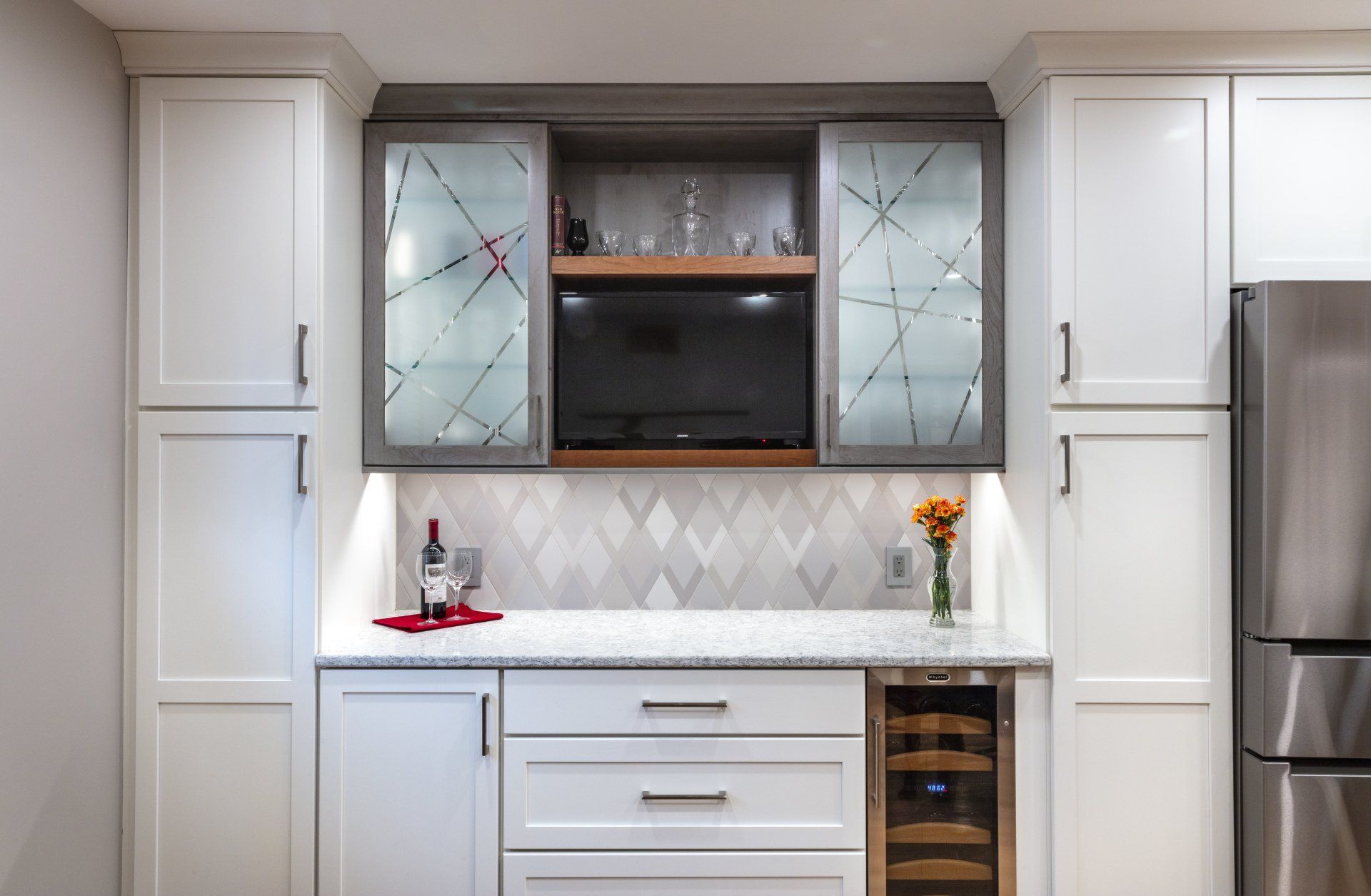 Modern white kitchen with glass-front cabinets, stainless fridge, and a built-in coffee/bar nook