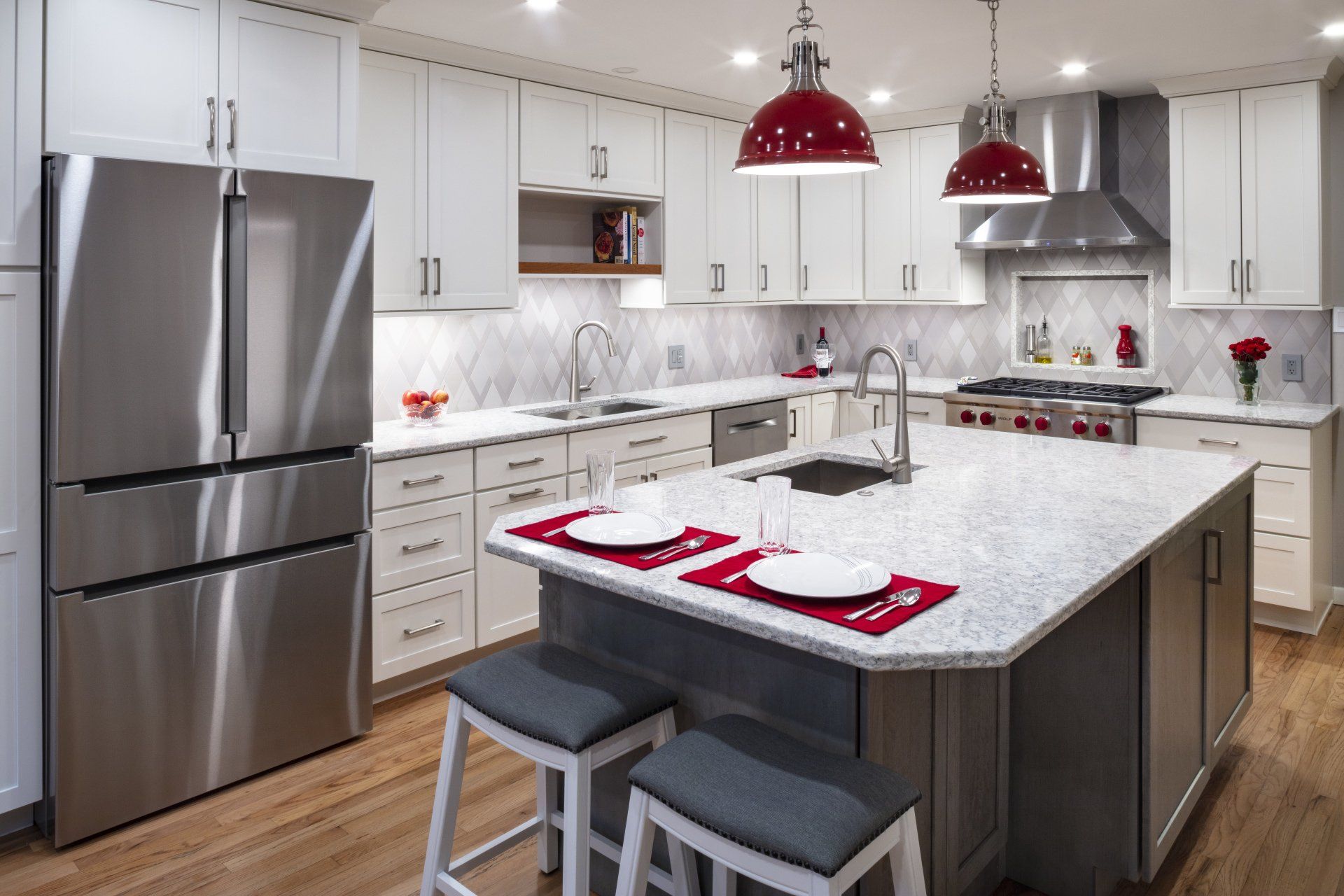 Modern kitchen with stainless steel appliances, white cabinets, marble island, and red pendant lights