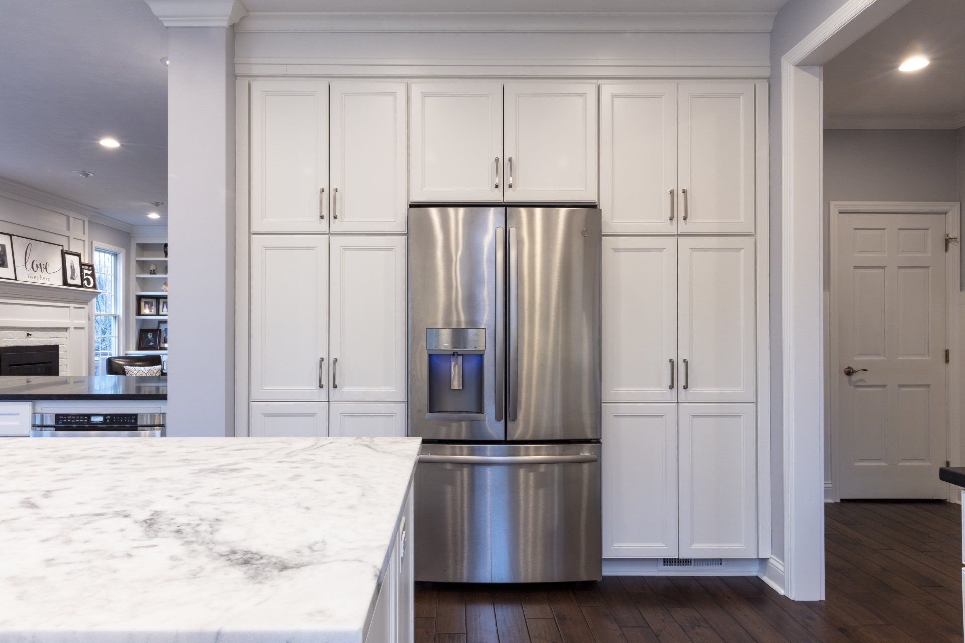 Modern white kitchen with stainless steel refrigerator and marble island countertop
