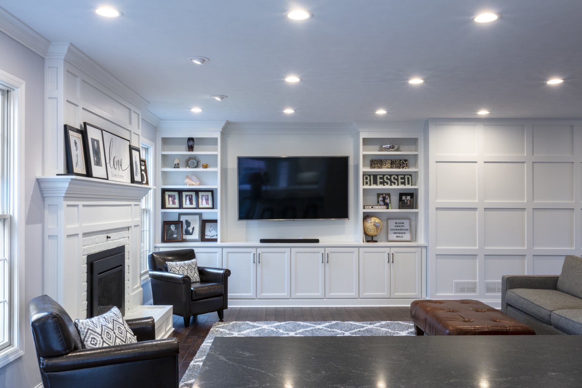Bright modern living room with wall-mounted TV, white built-ins, fireplace, and gray seating
