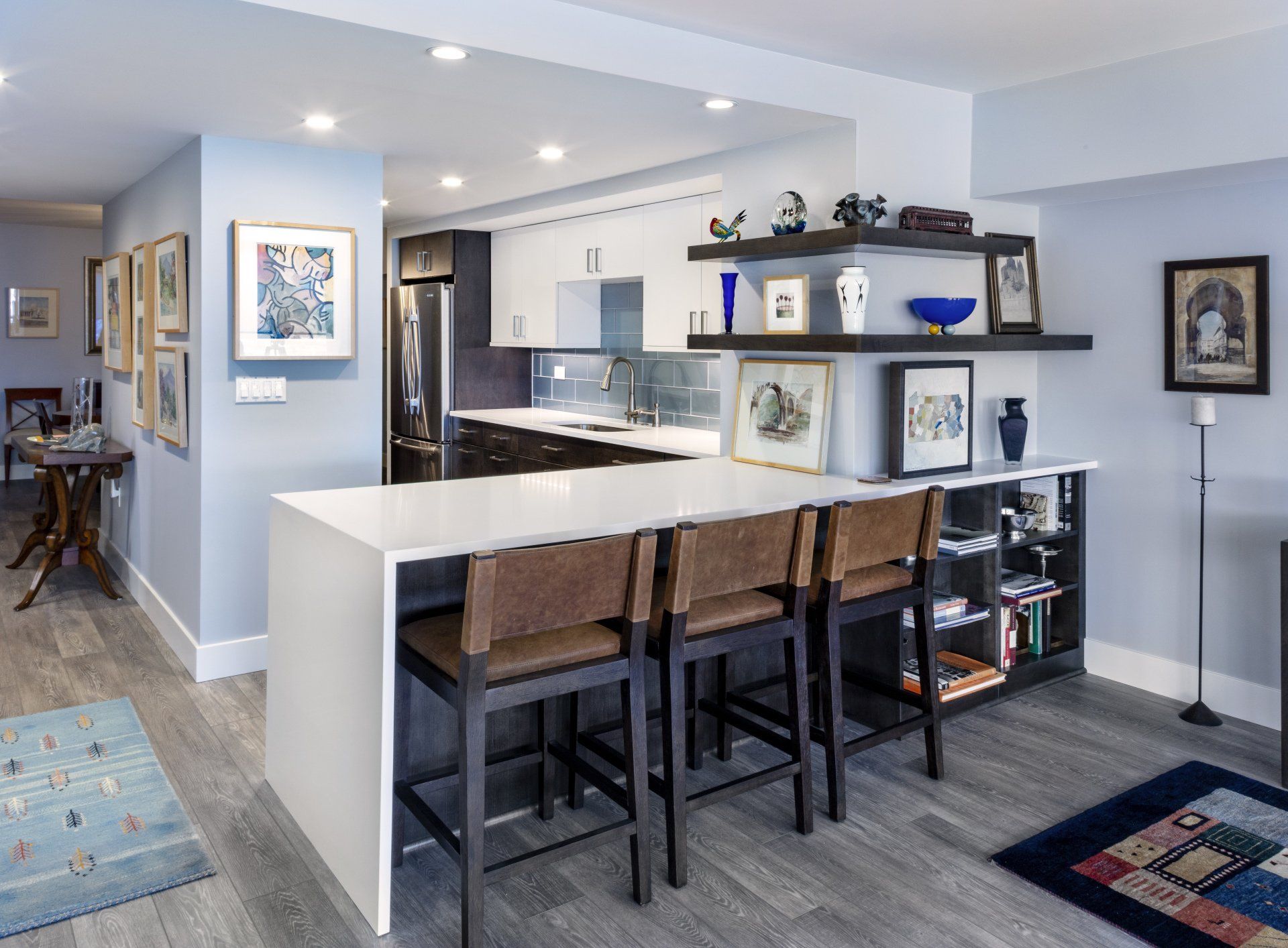 Modern open-concept kitchen with white island, barstools, and gray walls leading into a living area