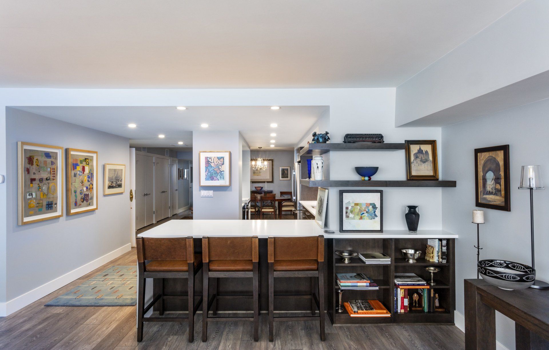 Modern open-concept living room with bar seating, shelves, framed art, and warm wood flooring