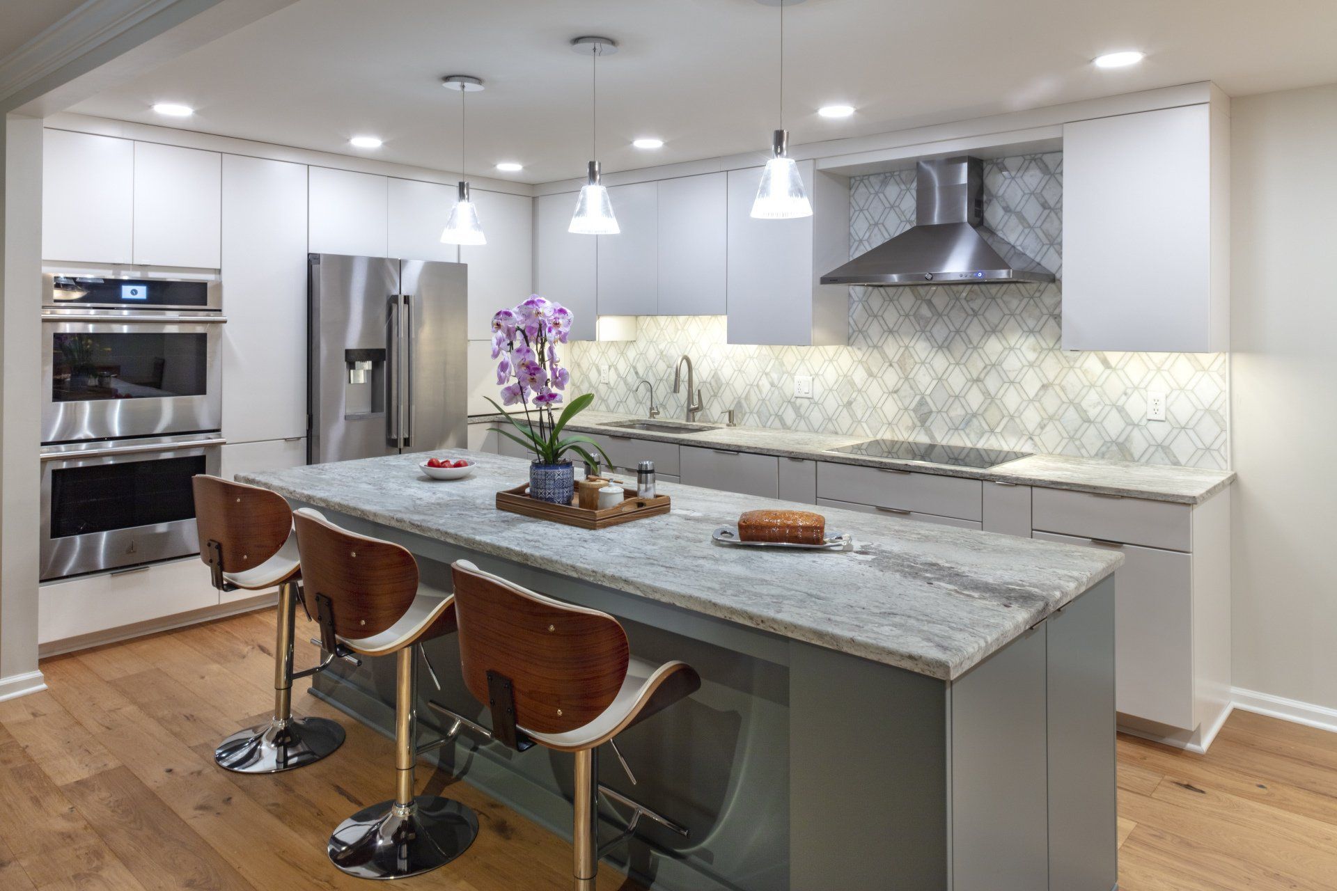 Modern kitchen with gray island, bar stools, pendant lights, stainless appliances, and white cabinets