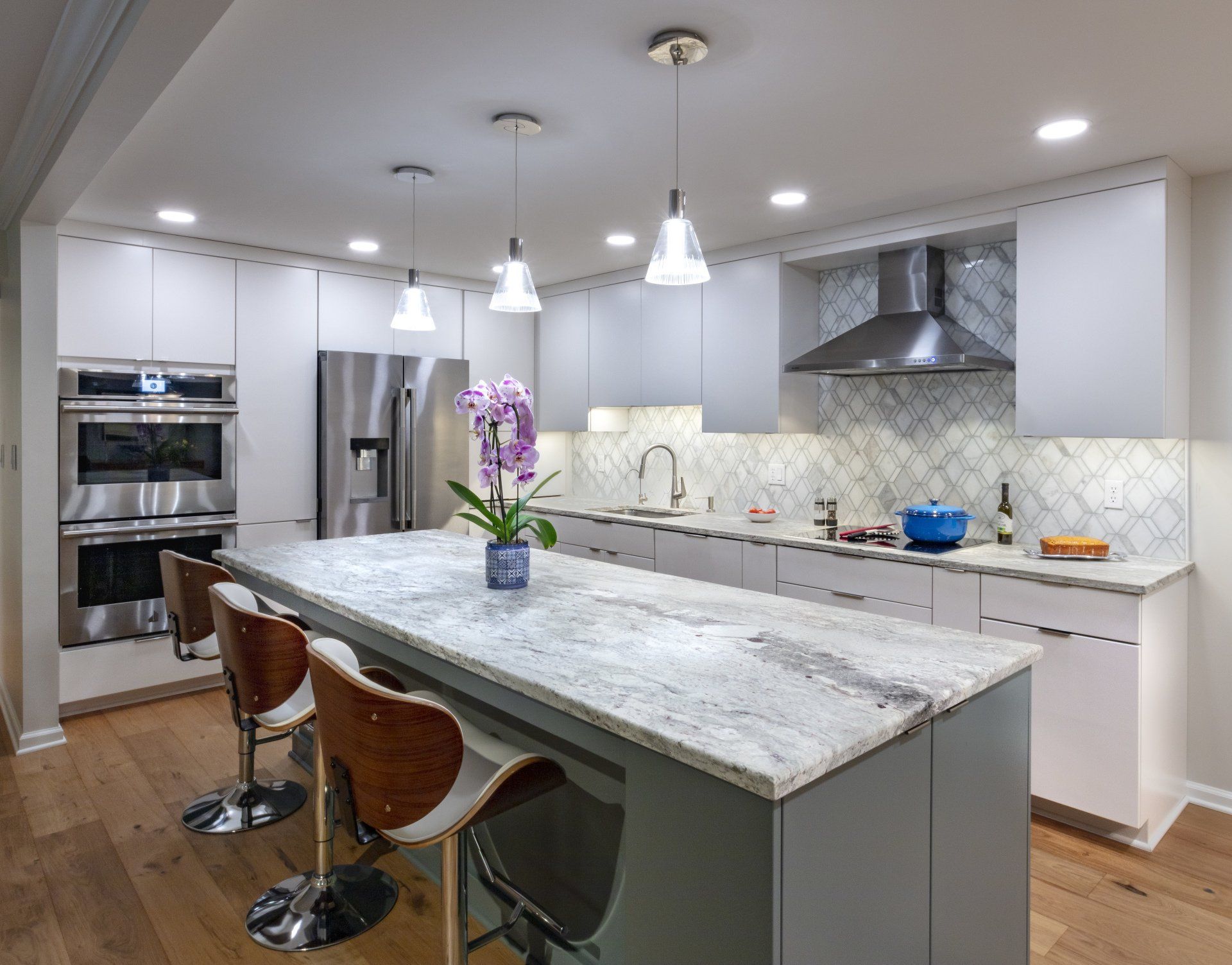 Modern white kitchen with marble island, pendant lights, stainless steel appliances, and wood bar stools
