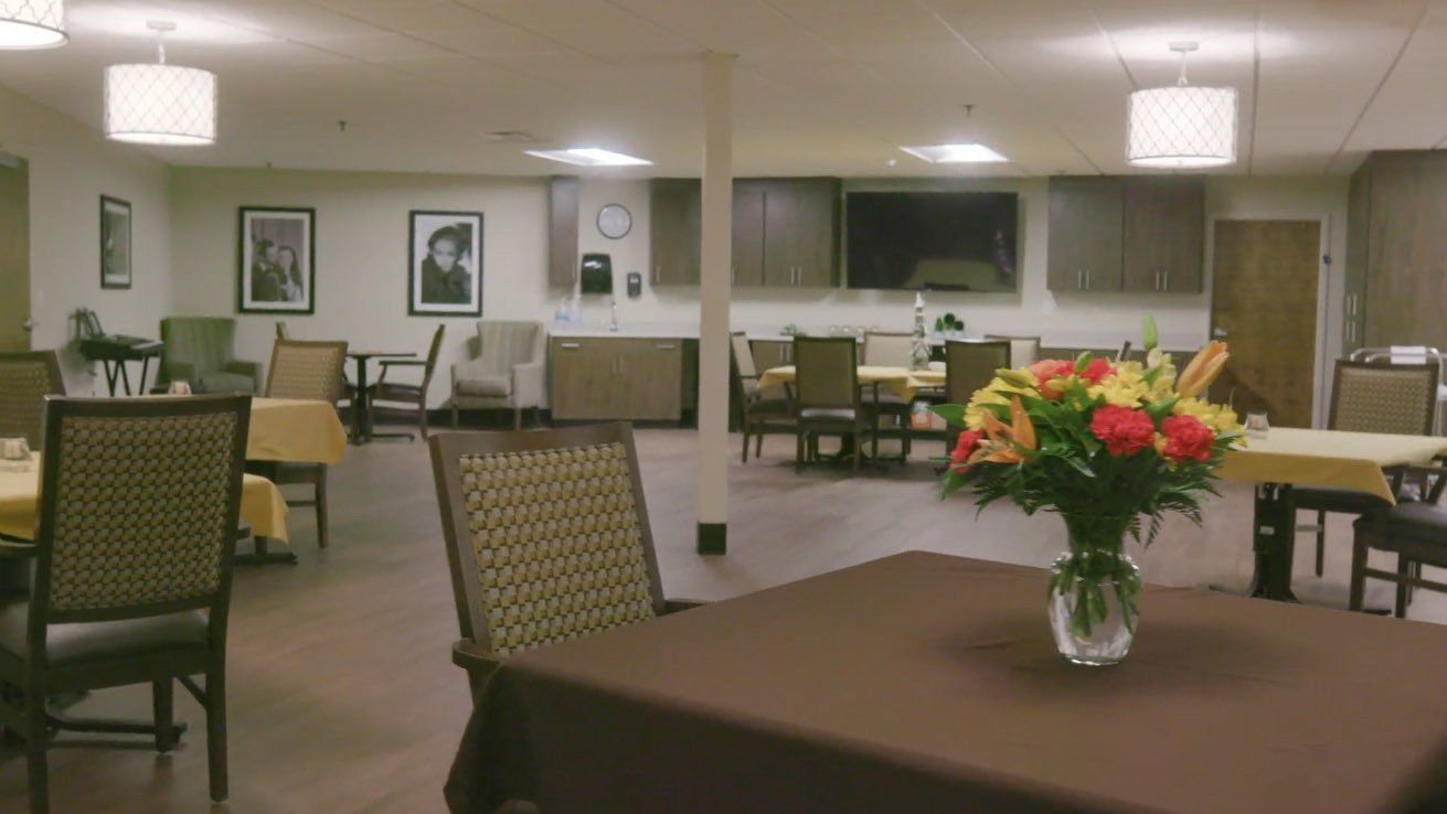 A dining room with tables and chairs and a vase of flowers on the table.