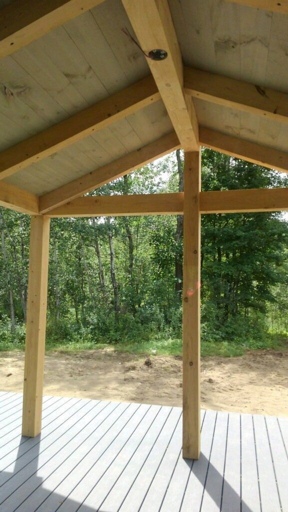 A wooden deck with a roof and trees in the background