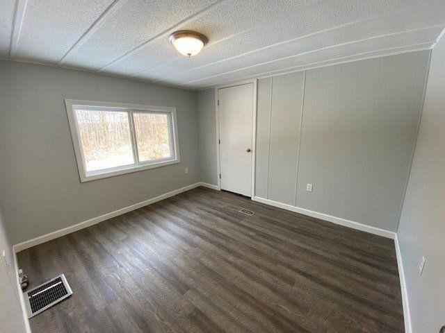 Empty room with light gray walls, window, door, and wood-look flooring. White ceiling with a light fixture.