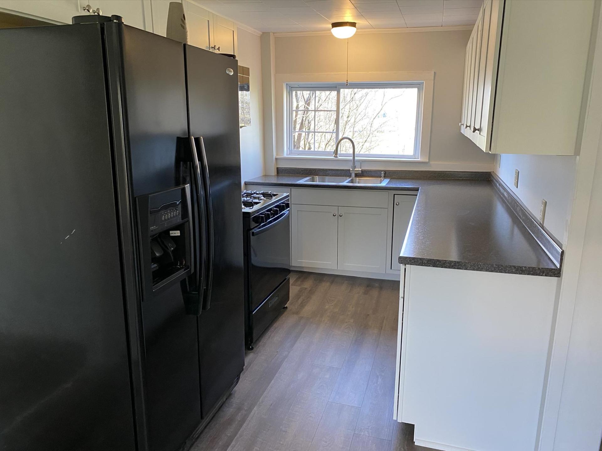 Black refrigerator and stove in a kitchen with white cabinets, light countertops, and a window.
