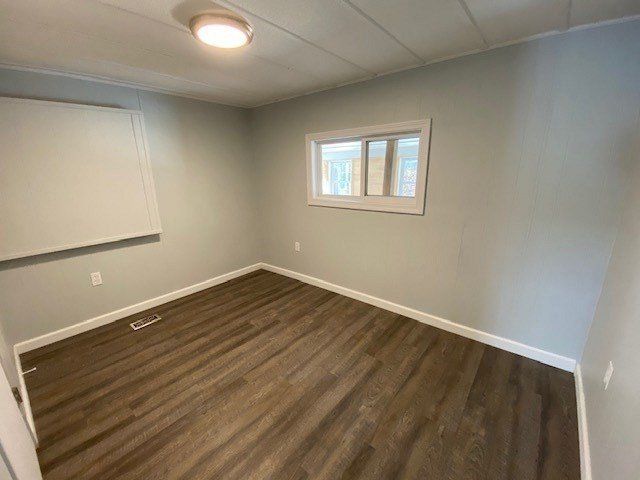 Empty bedroom with gray walls, wood-look flooring, and a small window.