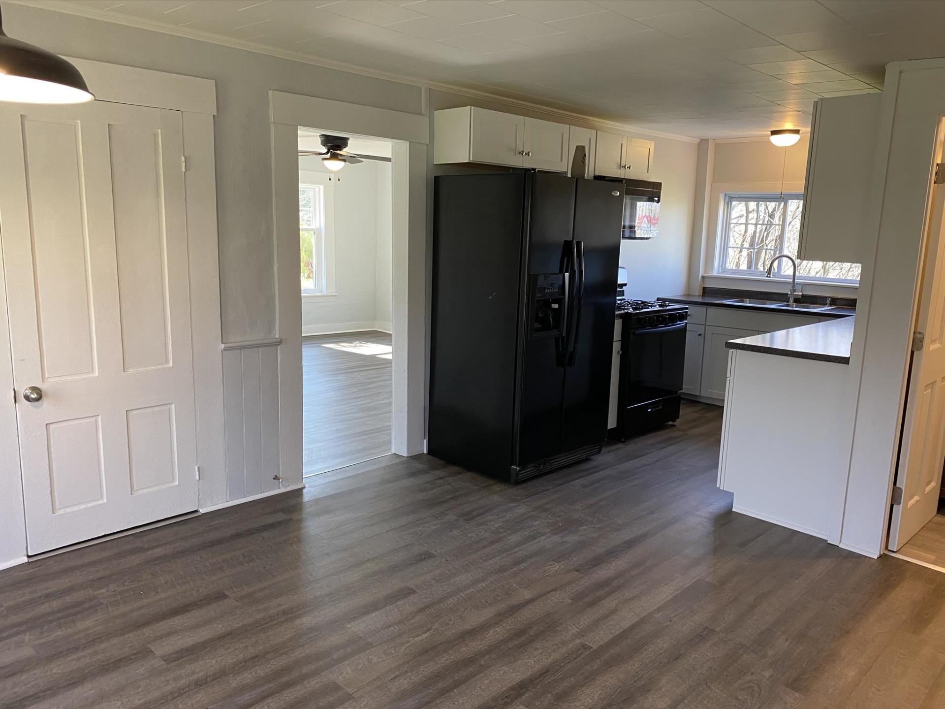 Kitchen with black refrigerator, white cabinets, and doorway to another room.