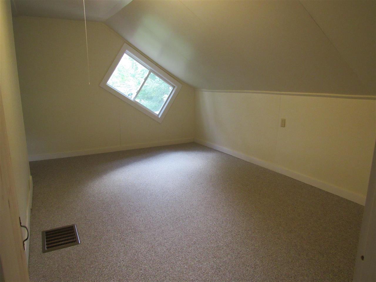 Empty room with sloped ceiling, window, carpeted floor, and beige walls.